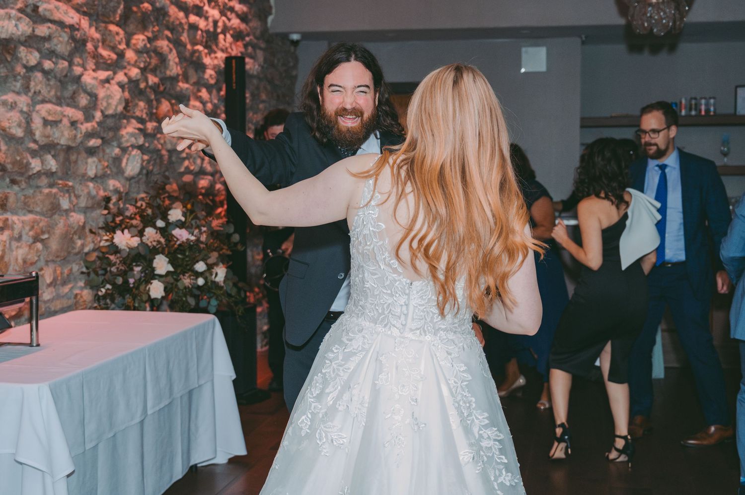 Newlyweds and guests dancing together during a joyful wedding reception celebration.