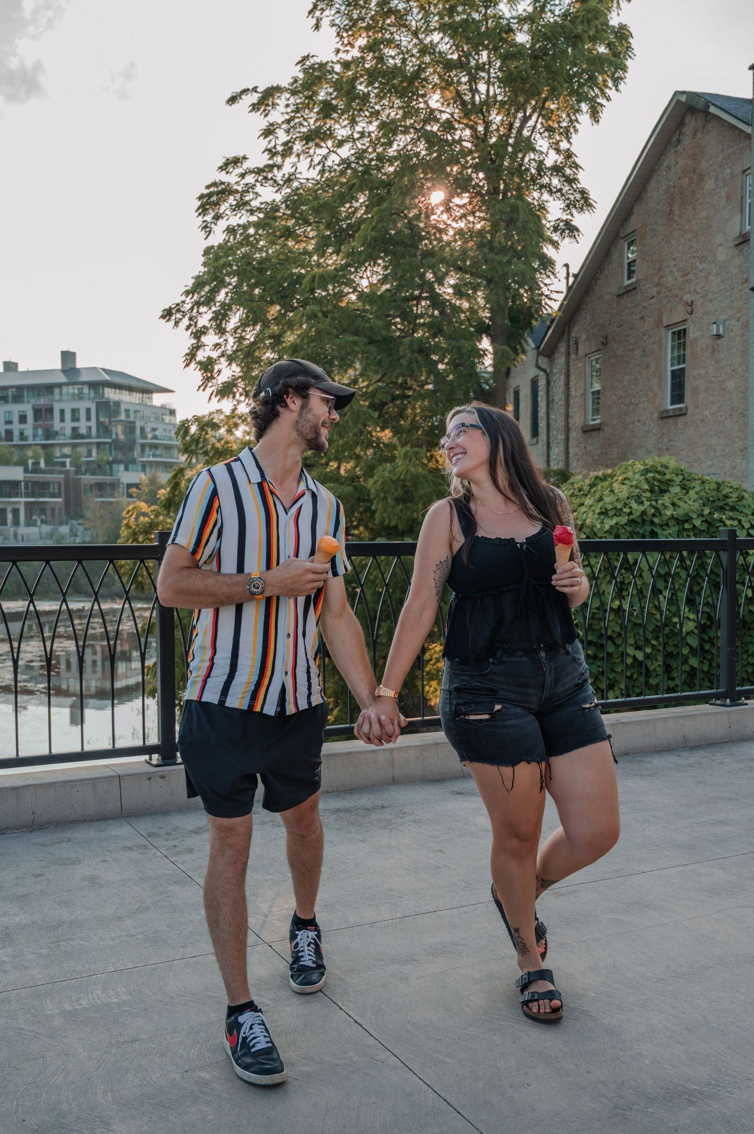 A couple in matching striped shirts and black shorts share playful dance moves on a downtown bridge in Elora.