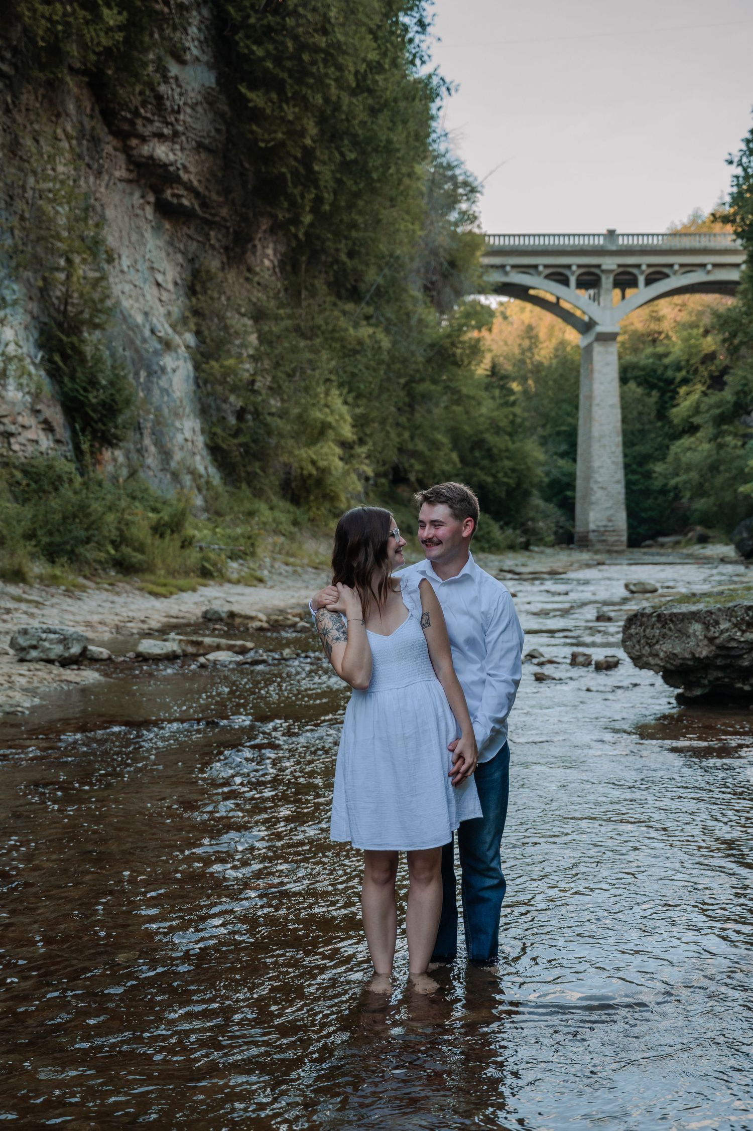 A couple enjoys a romantic moment while standing in shallow flowing water near the Elora Gorge Bridge.