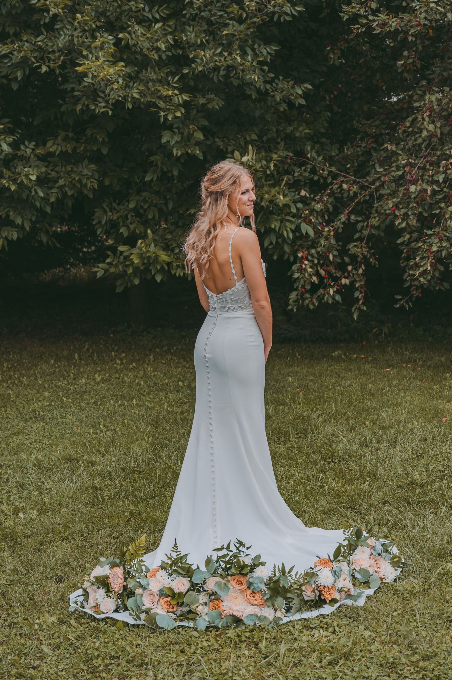 Back view of bride in fitted lace gown with floral train against garden backdrop.