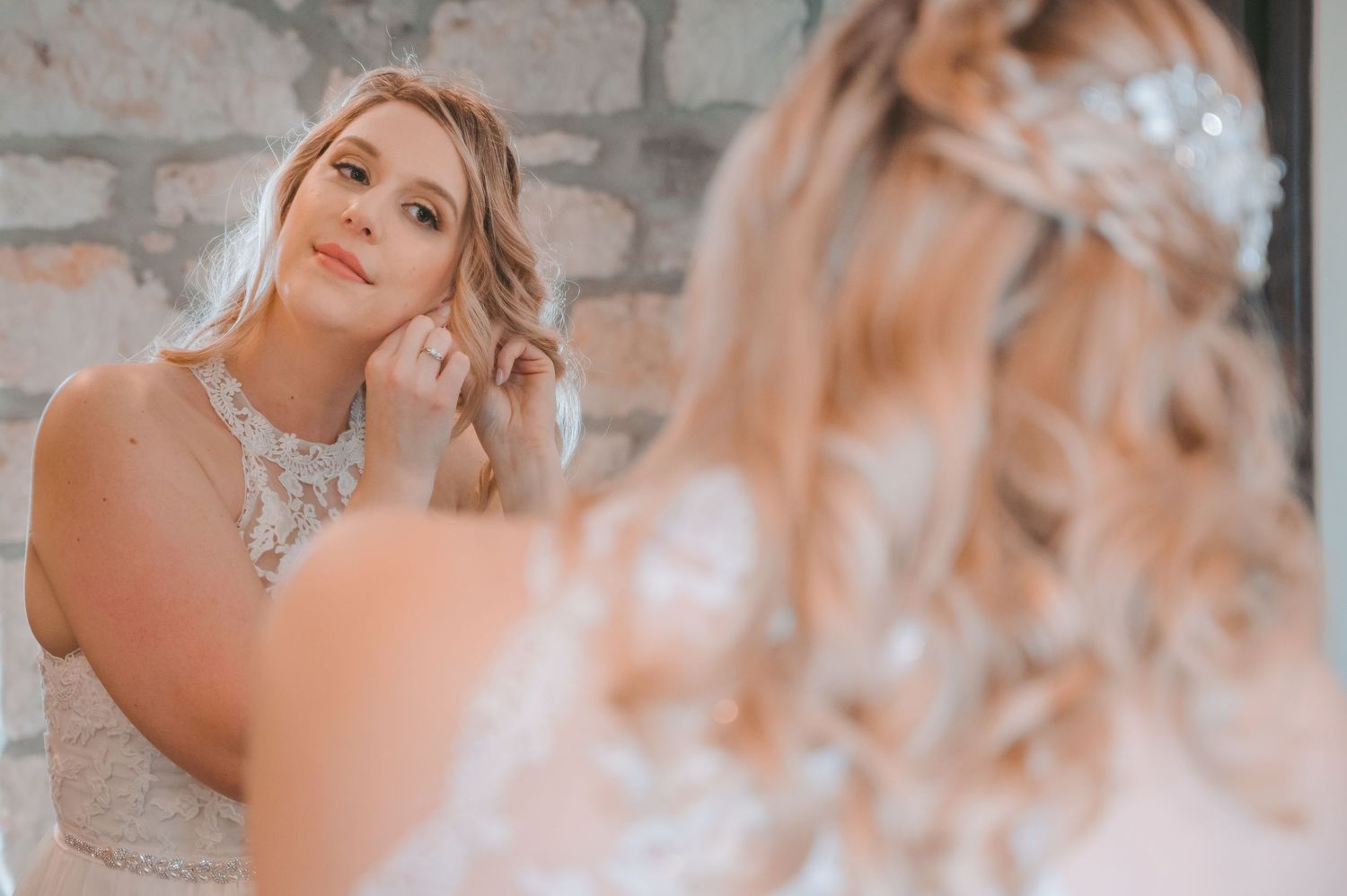 Bride getting ready while looking in mirror with soft lighting and stone wall background.