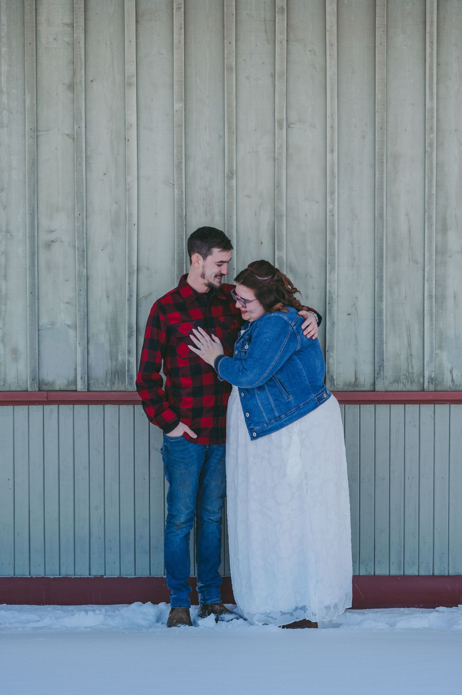 Couple embracing against industrial wall in winter setting.