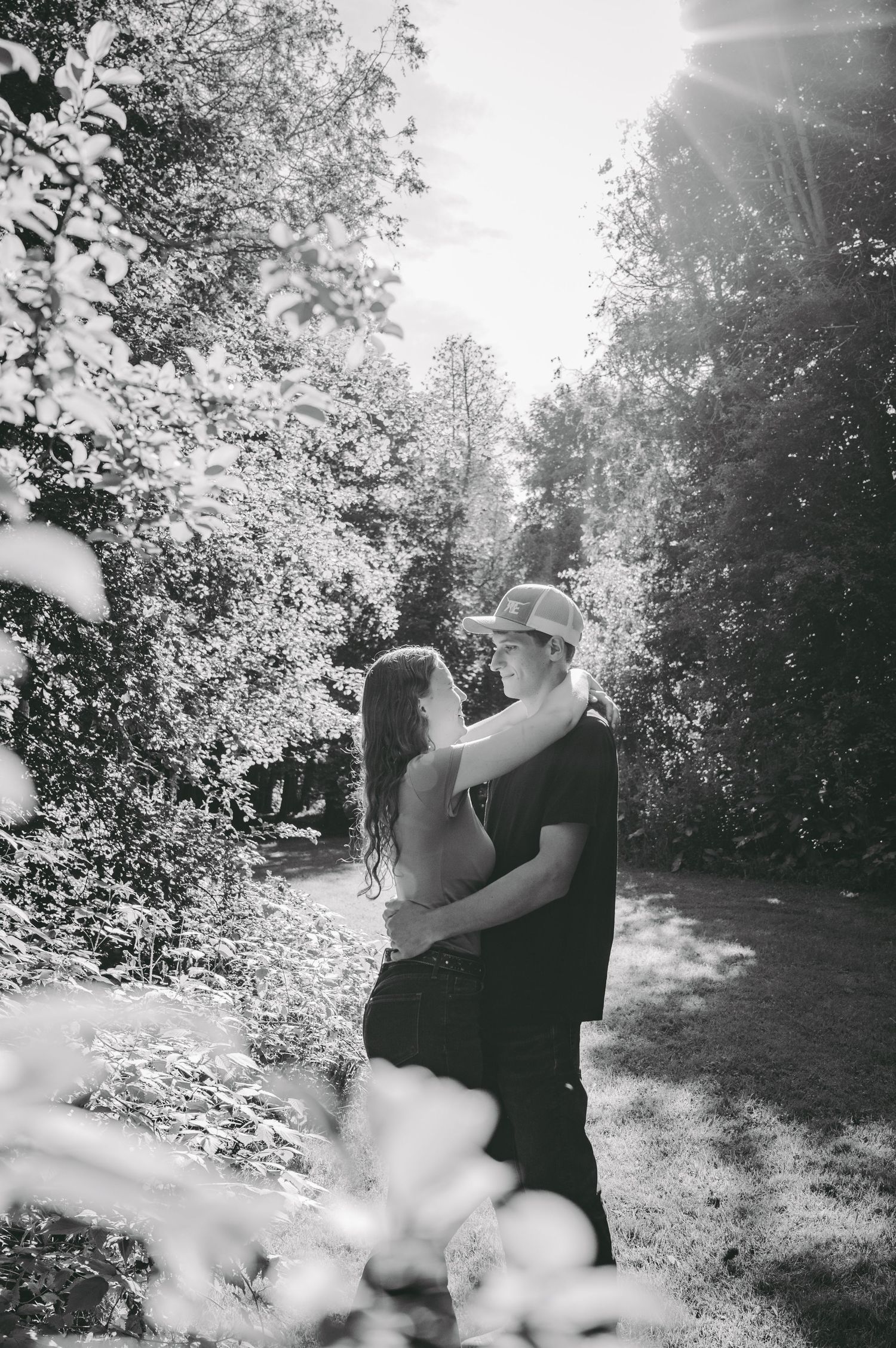 A romantic black and white photo with sunlight streaming through trees during an intimate moment.