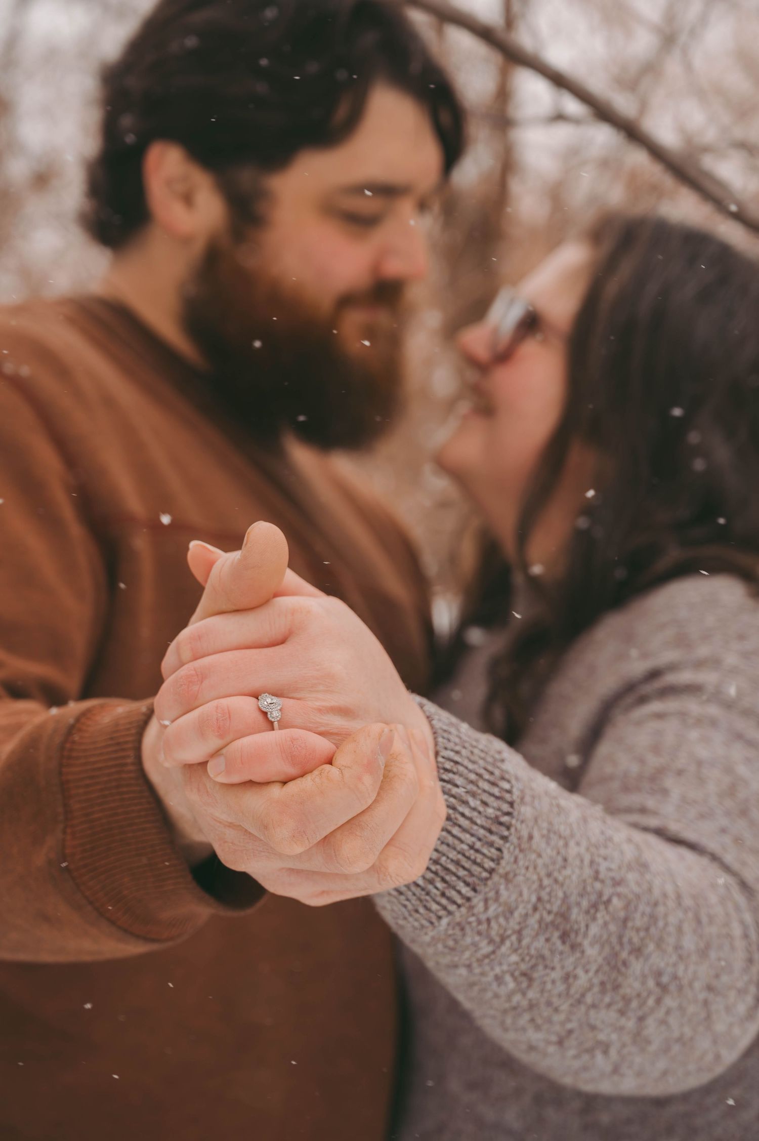 Close-up of couple holding hands in snow with engagement ring visible.