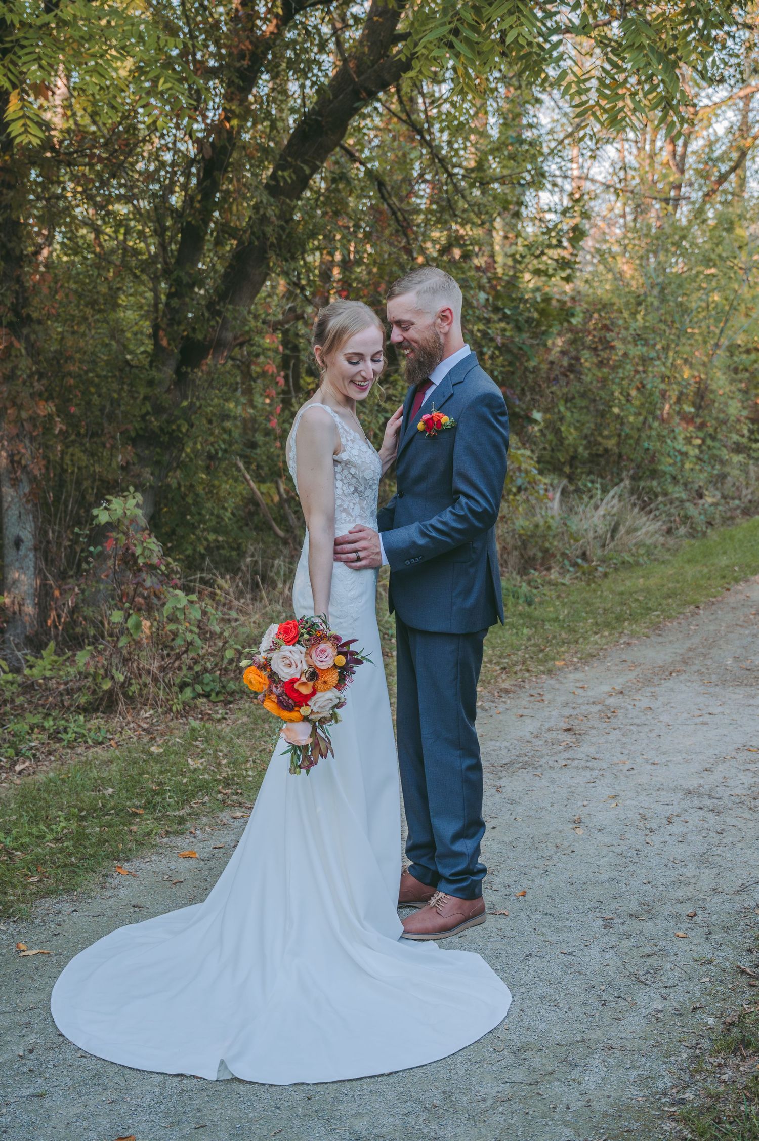 A couple in wedding attire shares an intimate moment on a gravel path during an autumn wedding.
