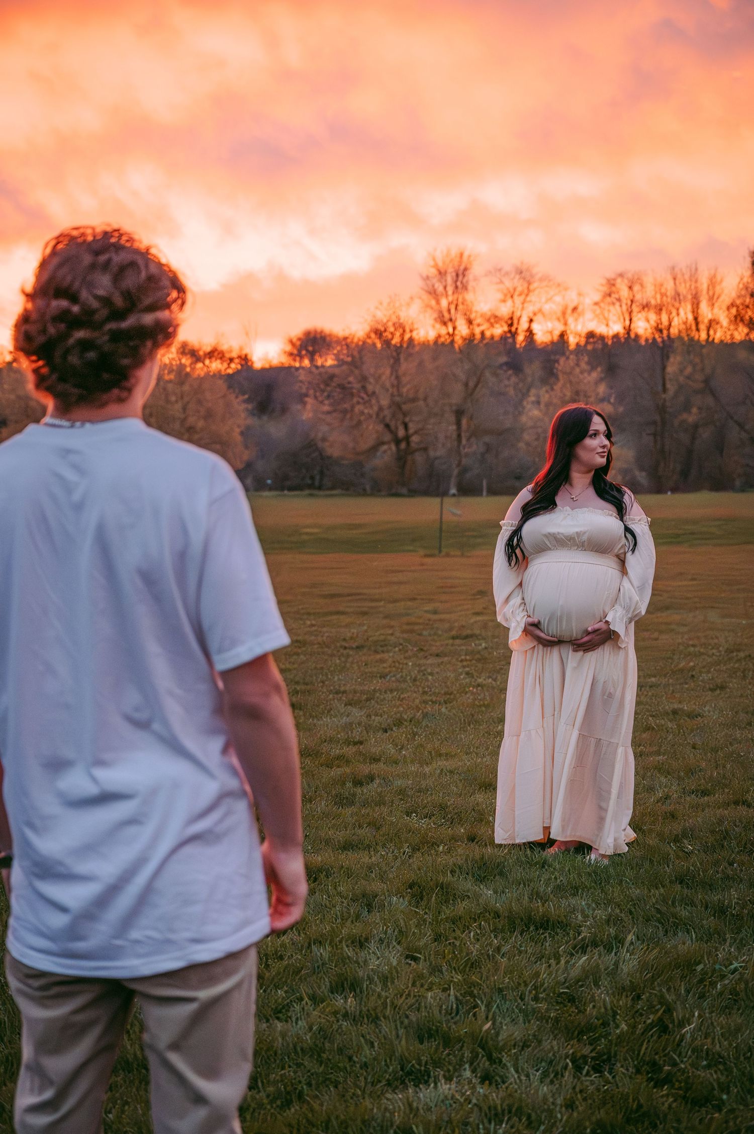 Sunset maternity session with couple standing apart in open field.