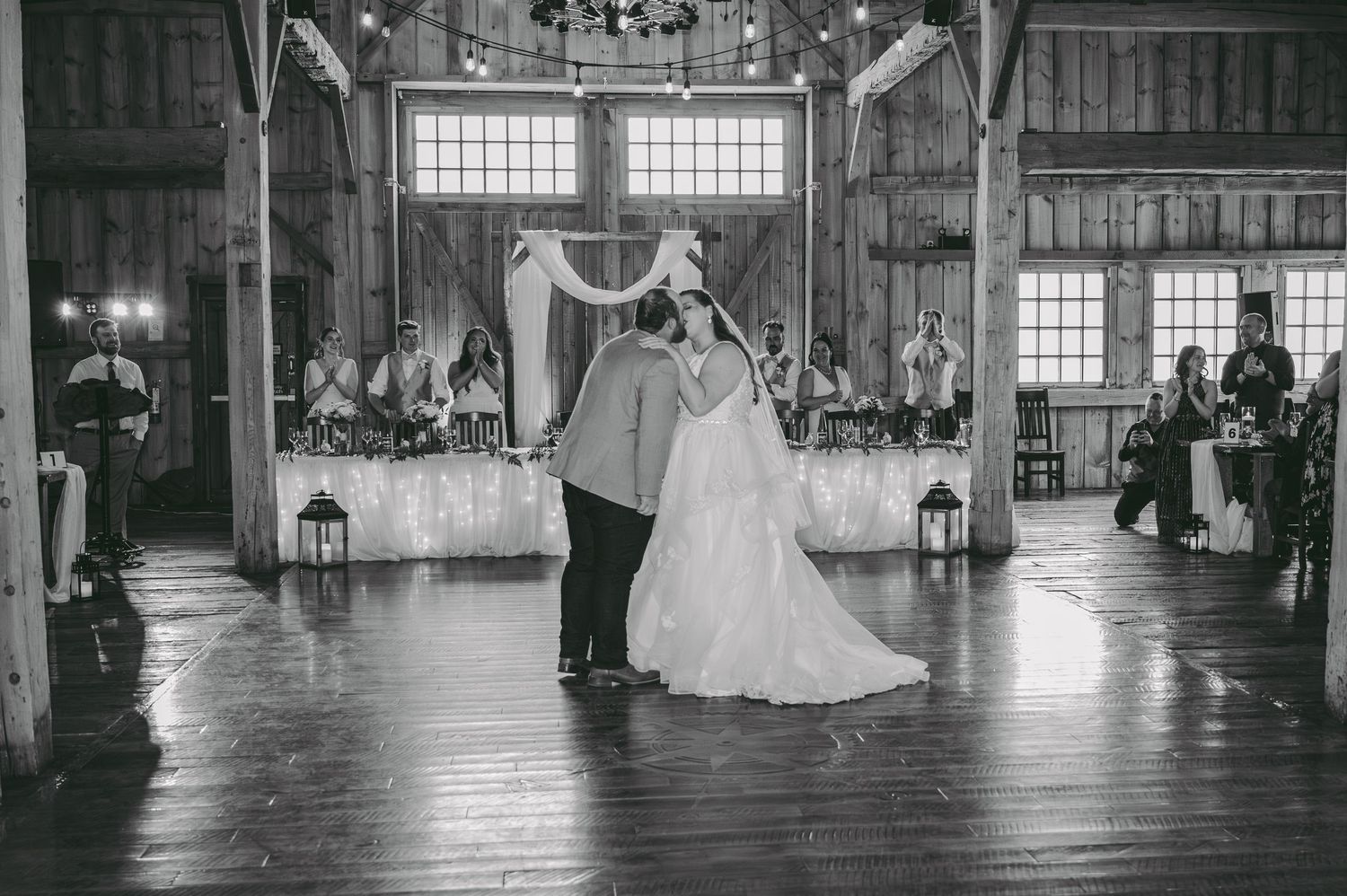 A couple shares their first dance in a beautifully lit rustic barn reception venue.