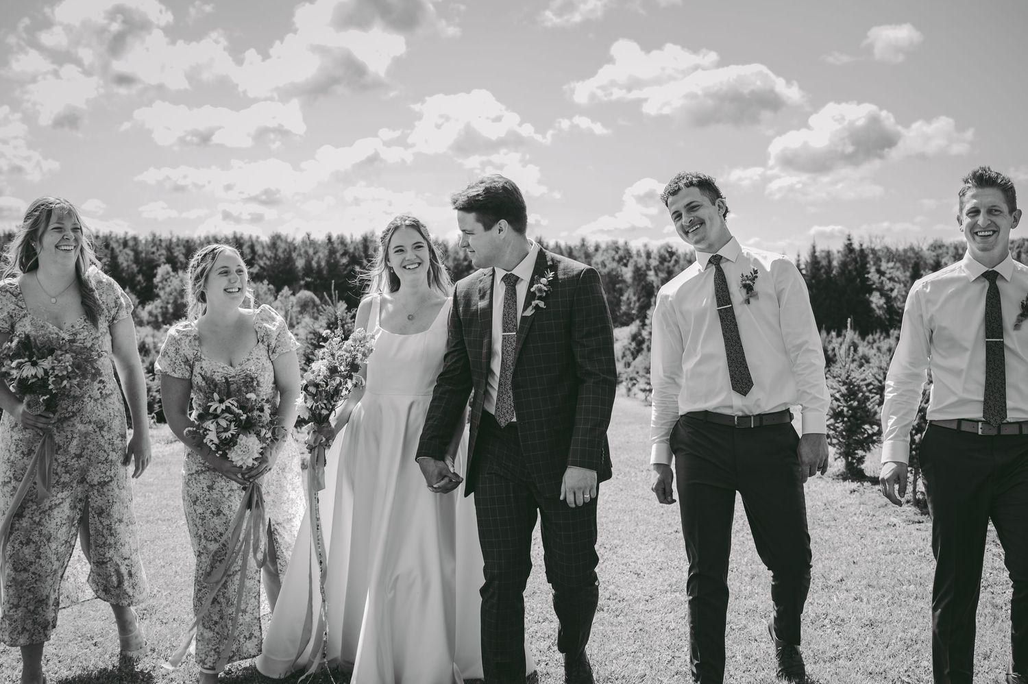 Black and white photo of wedding party laughing together outdoors.