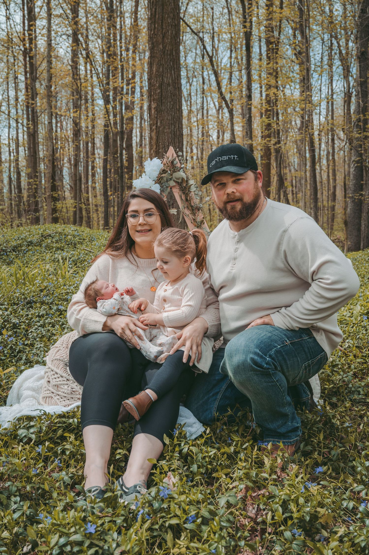 Family sitting together on moss-covered ground in an autumn forest setting.
