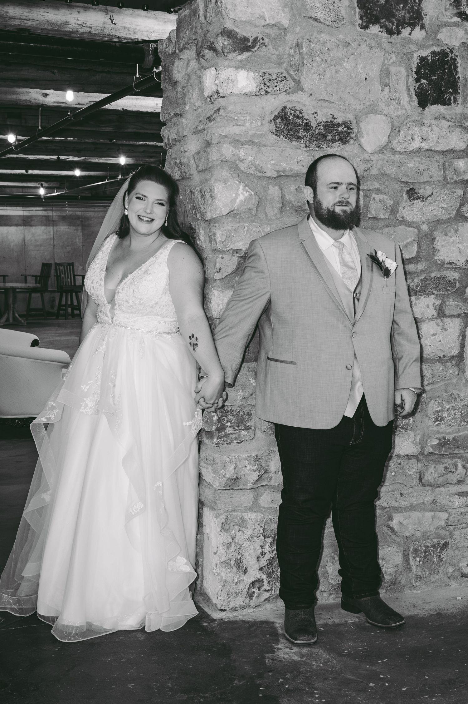 A wedding couple poses playfully against a rustic stone wall for their first touch.