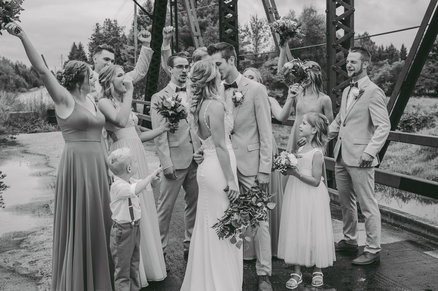 Black and white photo of wedding party celebrating on a rustic bridge.
