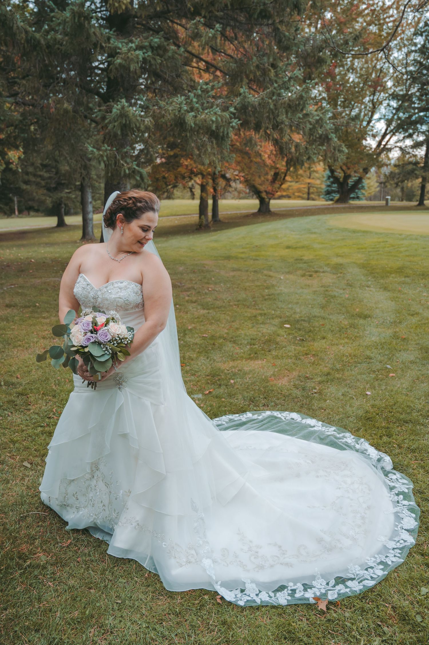 Bride in lace wedding gown with long train poses in autumn landscape.
