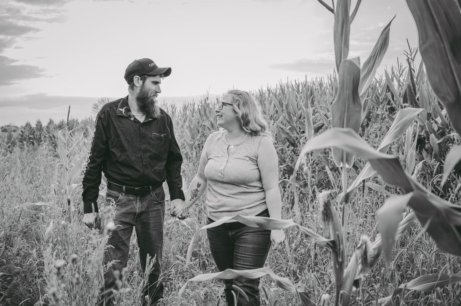 A couple walks through a cornfield together in black and white photography.