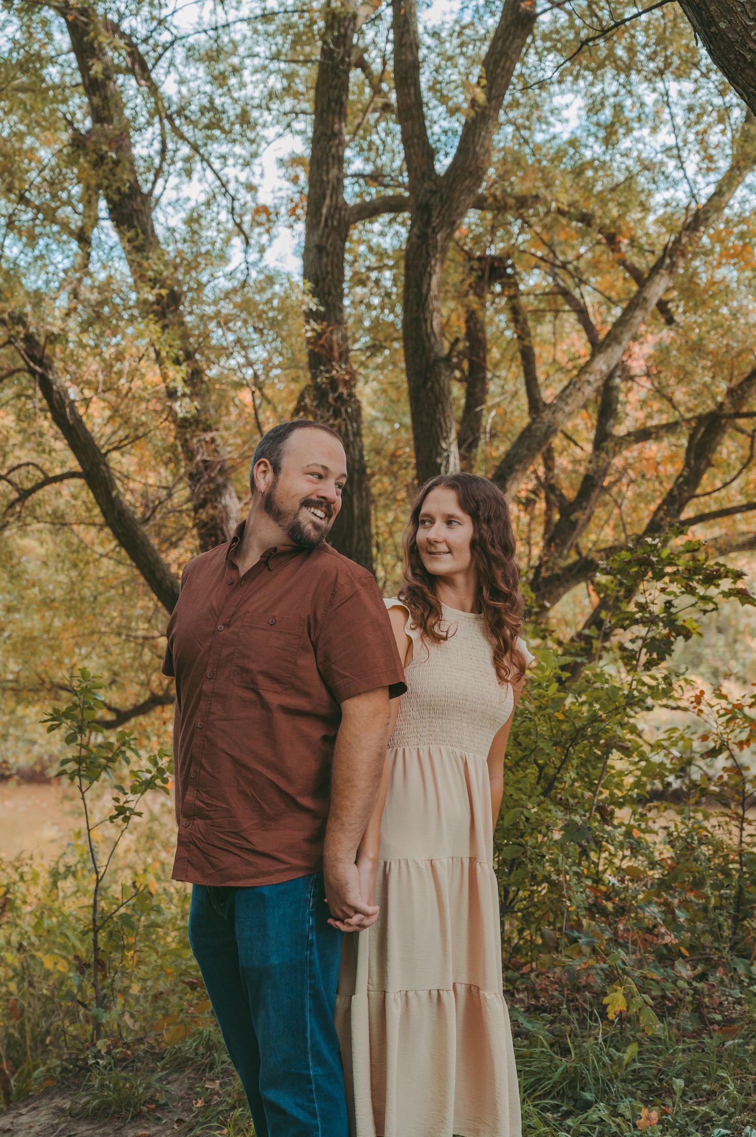 A couple shares a candid moment while standing under golden autumn trees.