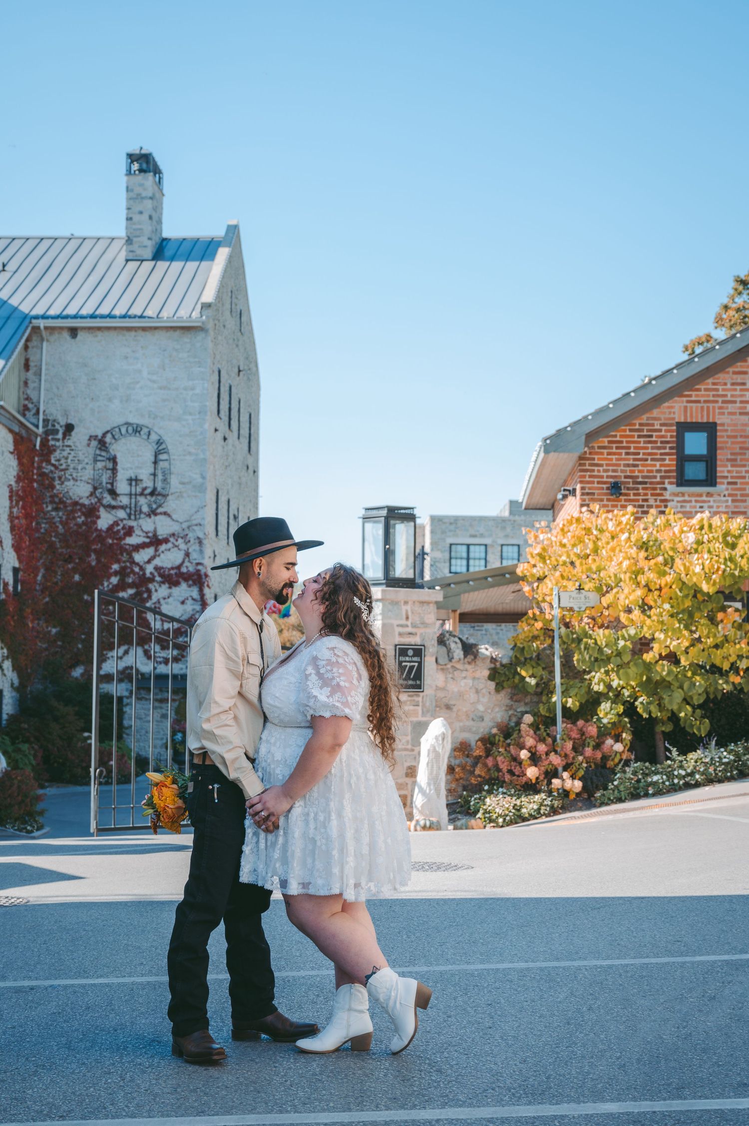 Couple in vintage-inspired wedding attire pose together on urban street with historic buildings.
