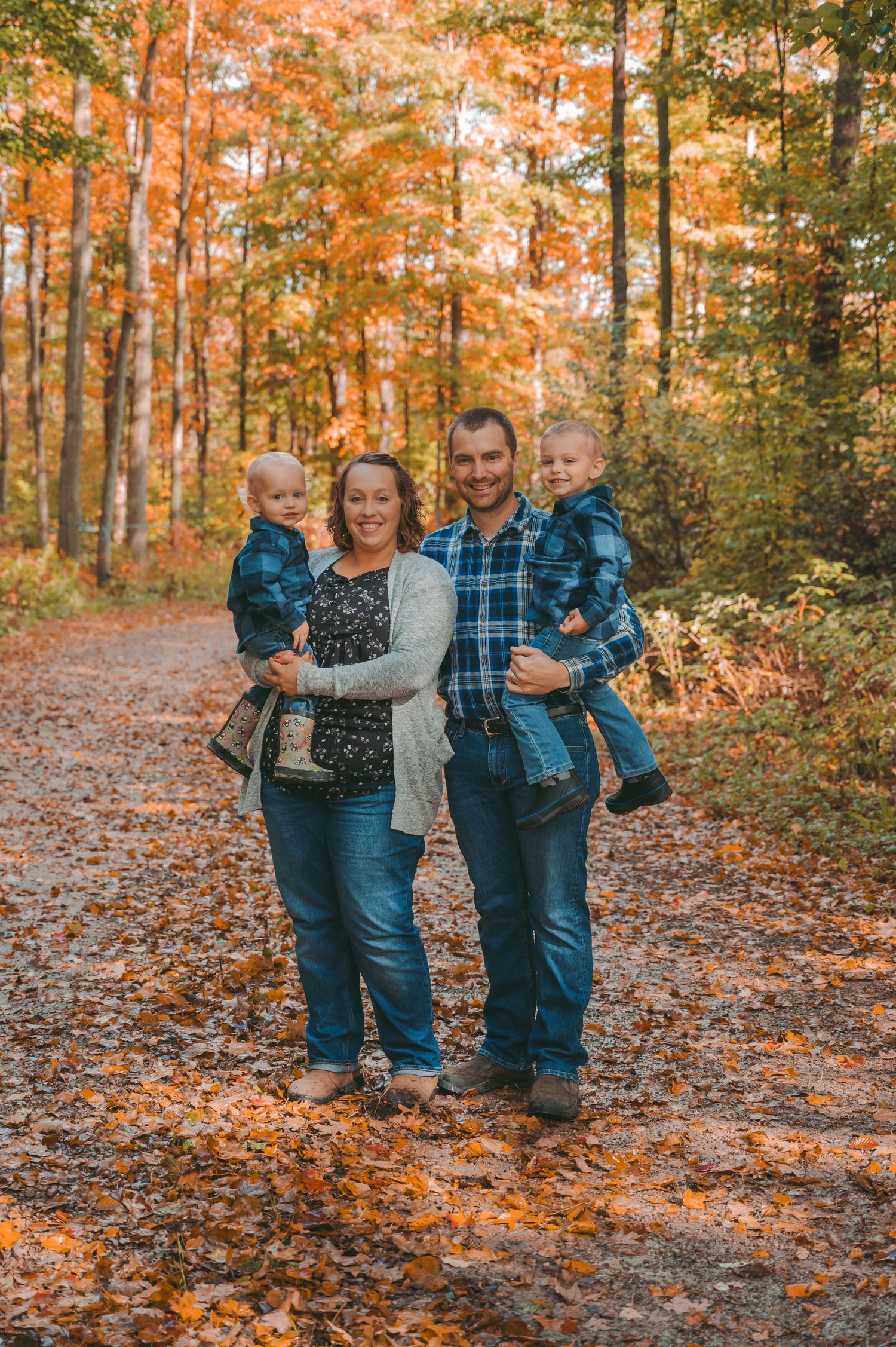 Family of four poses on autumn trail surrounded by orange and yellow foliage.