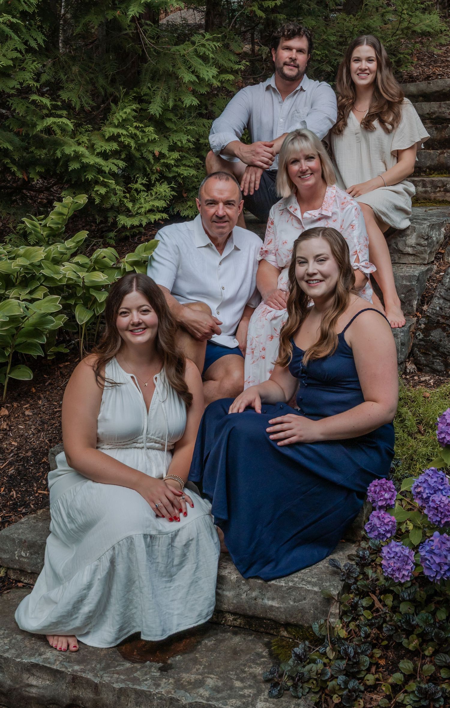 Family photo session on stone steps with blooming purple hydrangeas in natural garden setting.