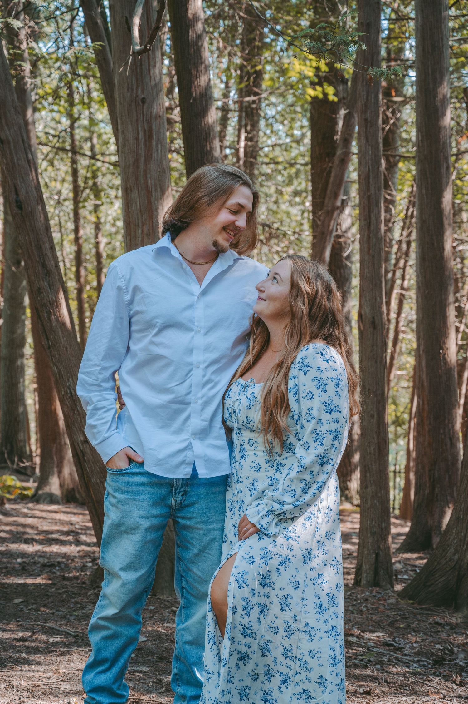 A couple in coordinating blue outfits share an intimate moment in a wooded setting.