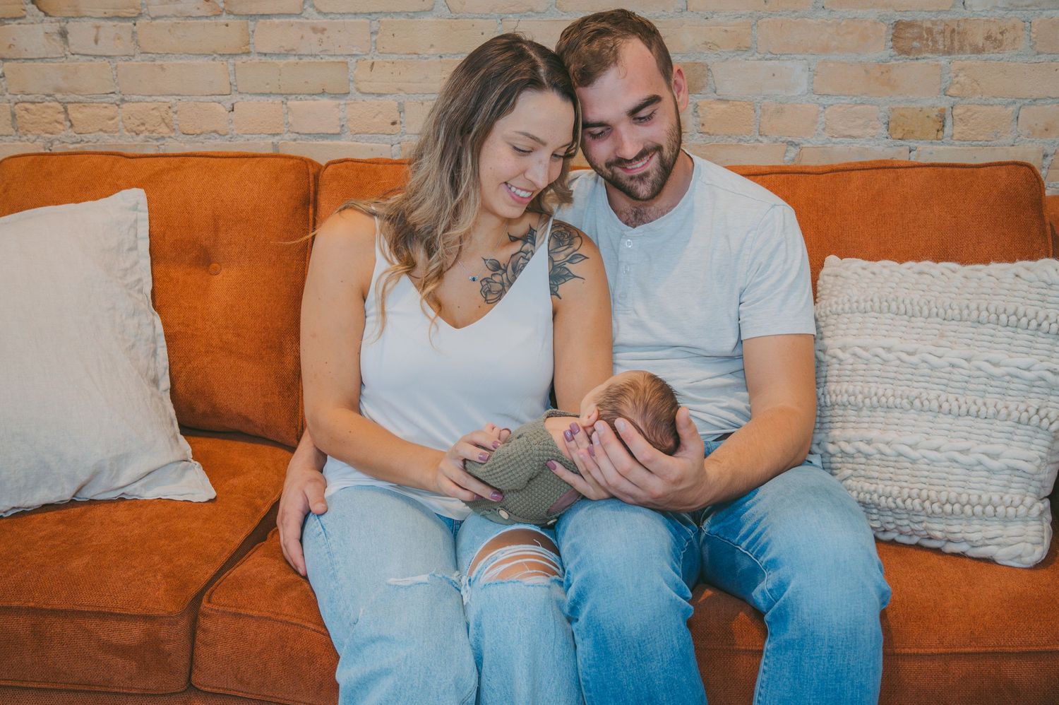 Couple sharing a tender moment while sitting on an orange couch looking at their newborn together.