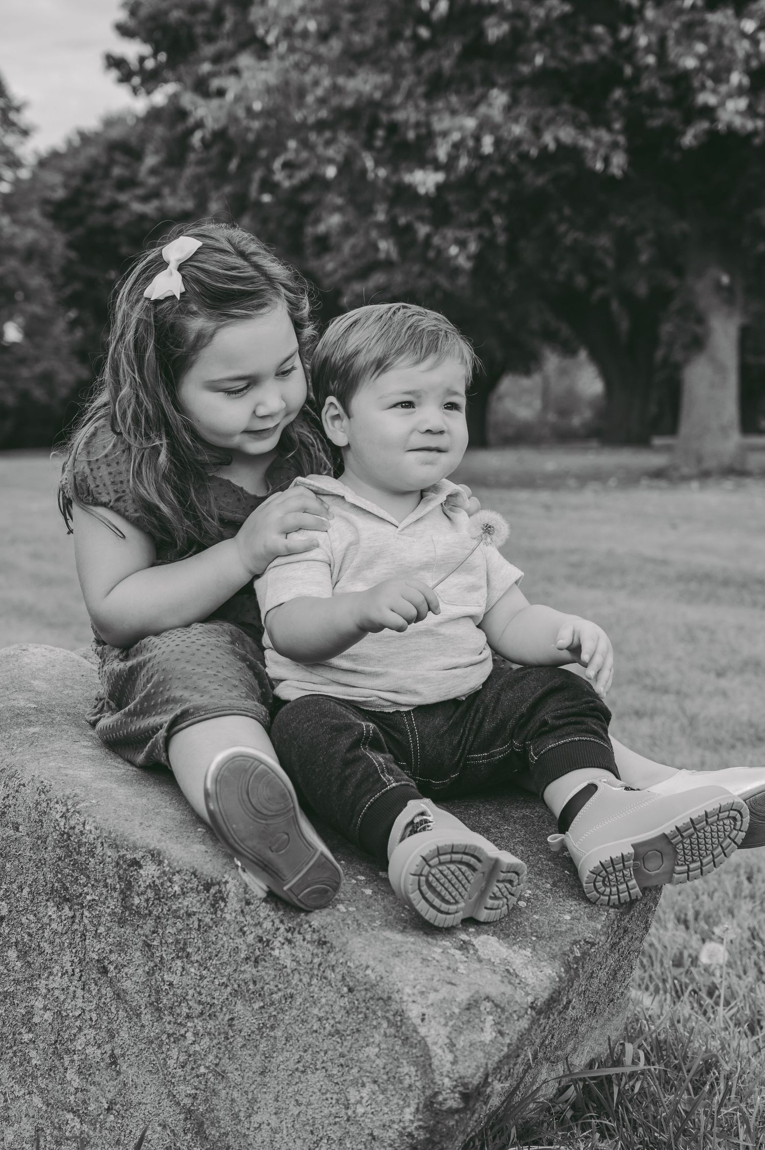 Black and white portrait of siblings sitting together on grassy ground.