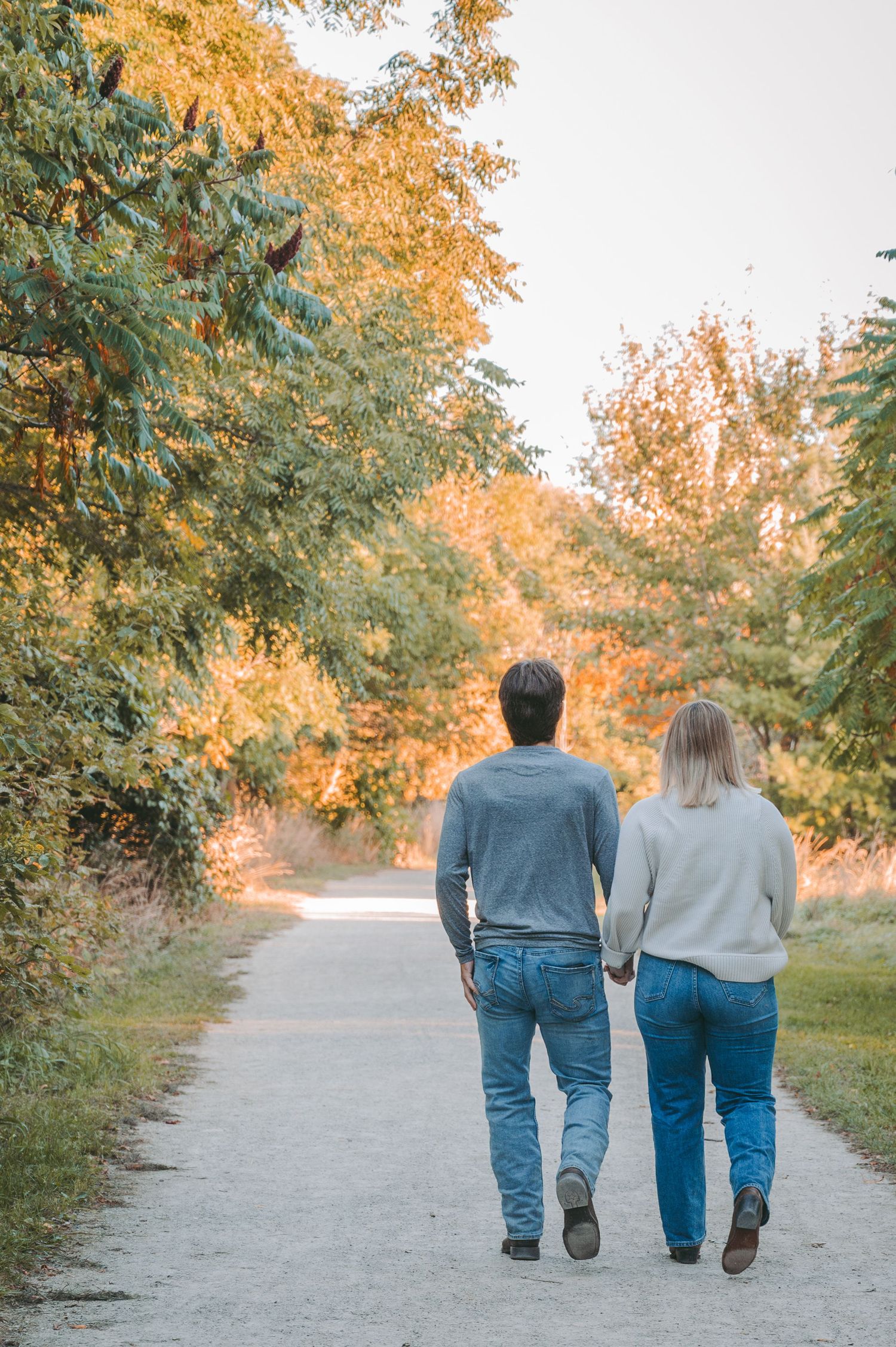 A couple walking hand in hand on a path surrounded by autumn trees with golden foliage.