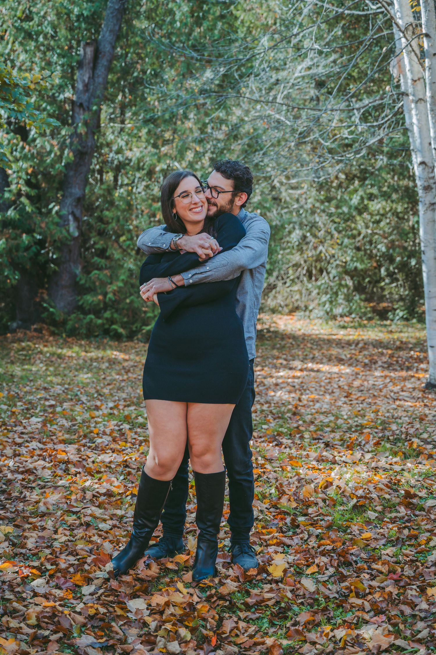 A couple embraces while sharing a laugh on fallen autumn leaves in a forest.