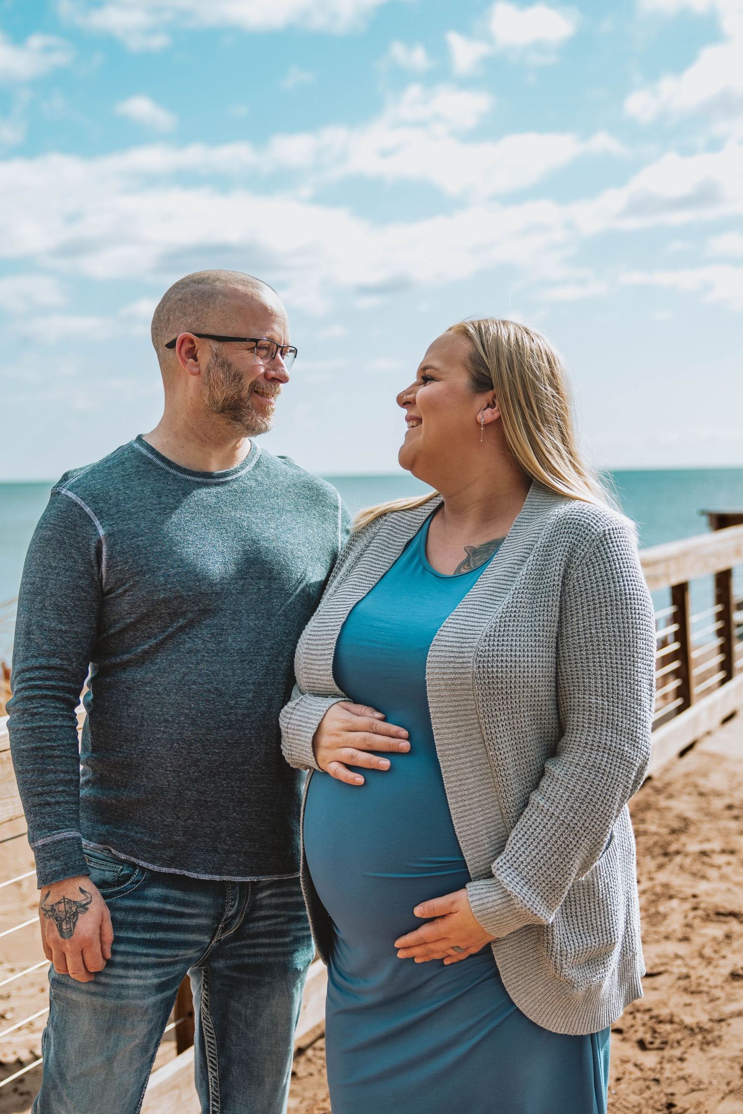 A couple sharing a tender moment on a boardwalk by the ocean on a sunny day.