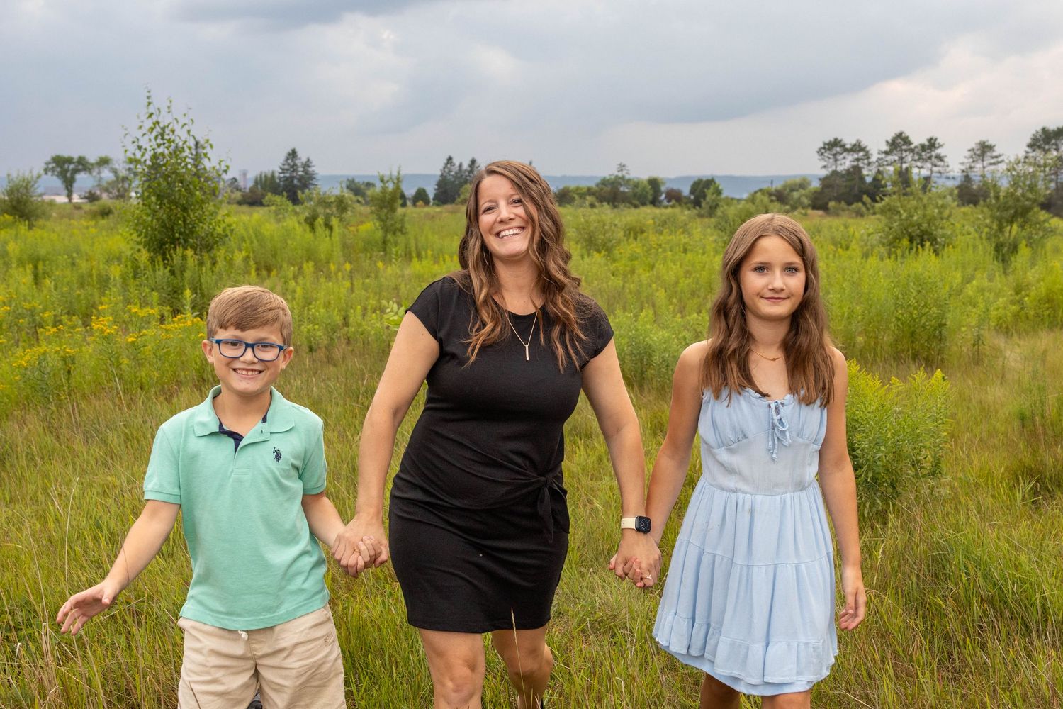 Family members laugh and play together in a sunny meadow with tall grass and trees in the background.
