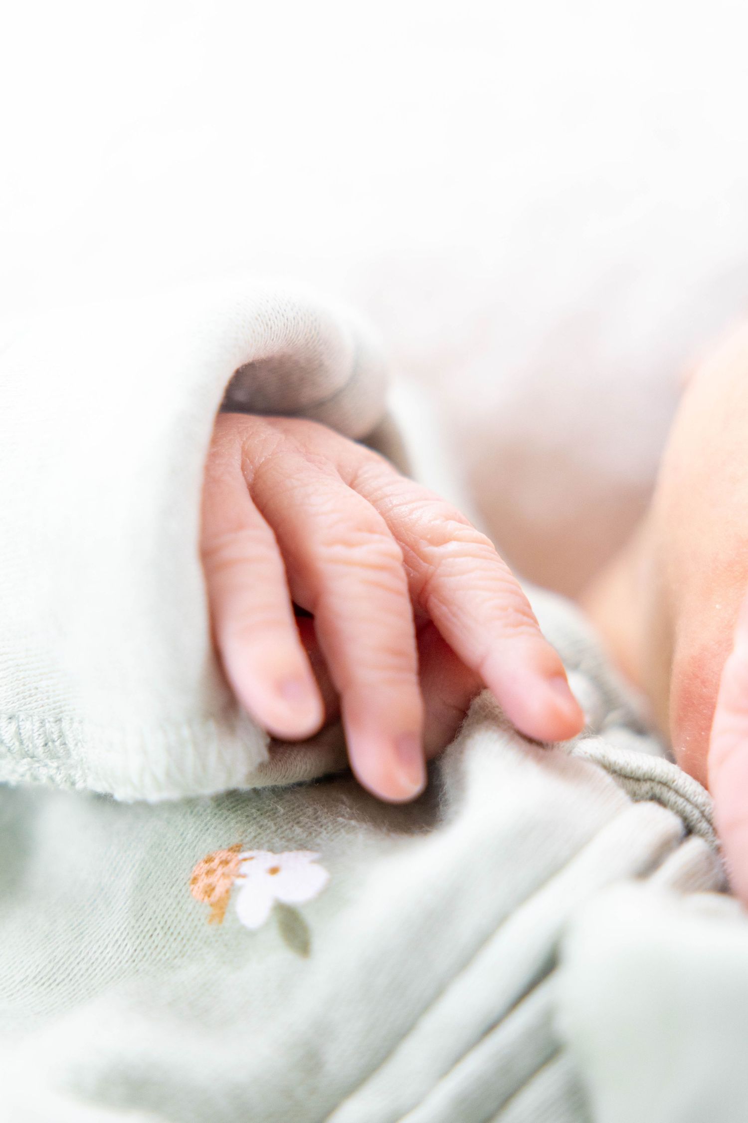 Delicate newborn hand grasping white embroidered fabric.