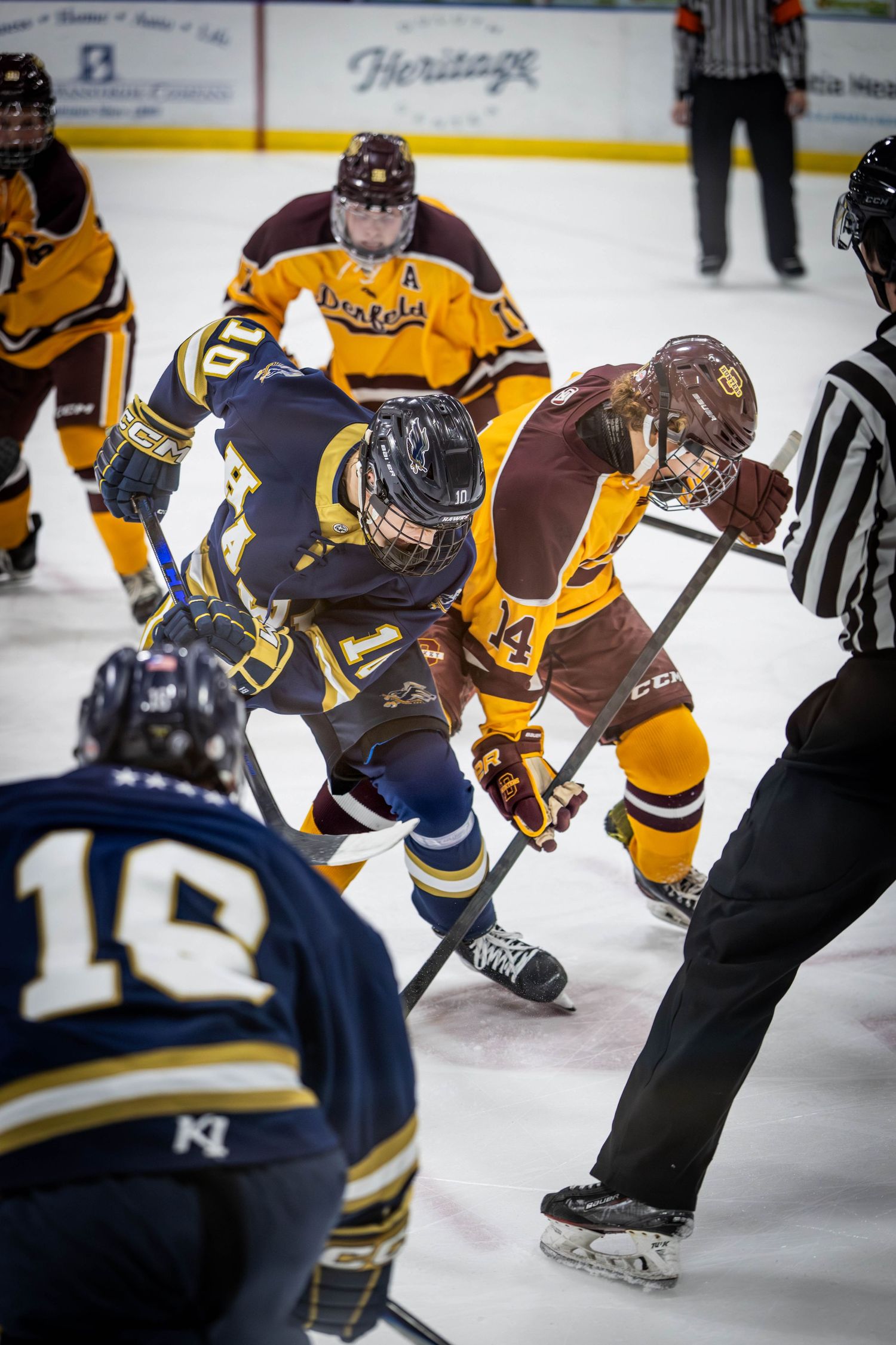 Hockey players face off on ice during a competitive game, with referees and teammates watching nearby.