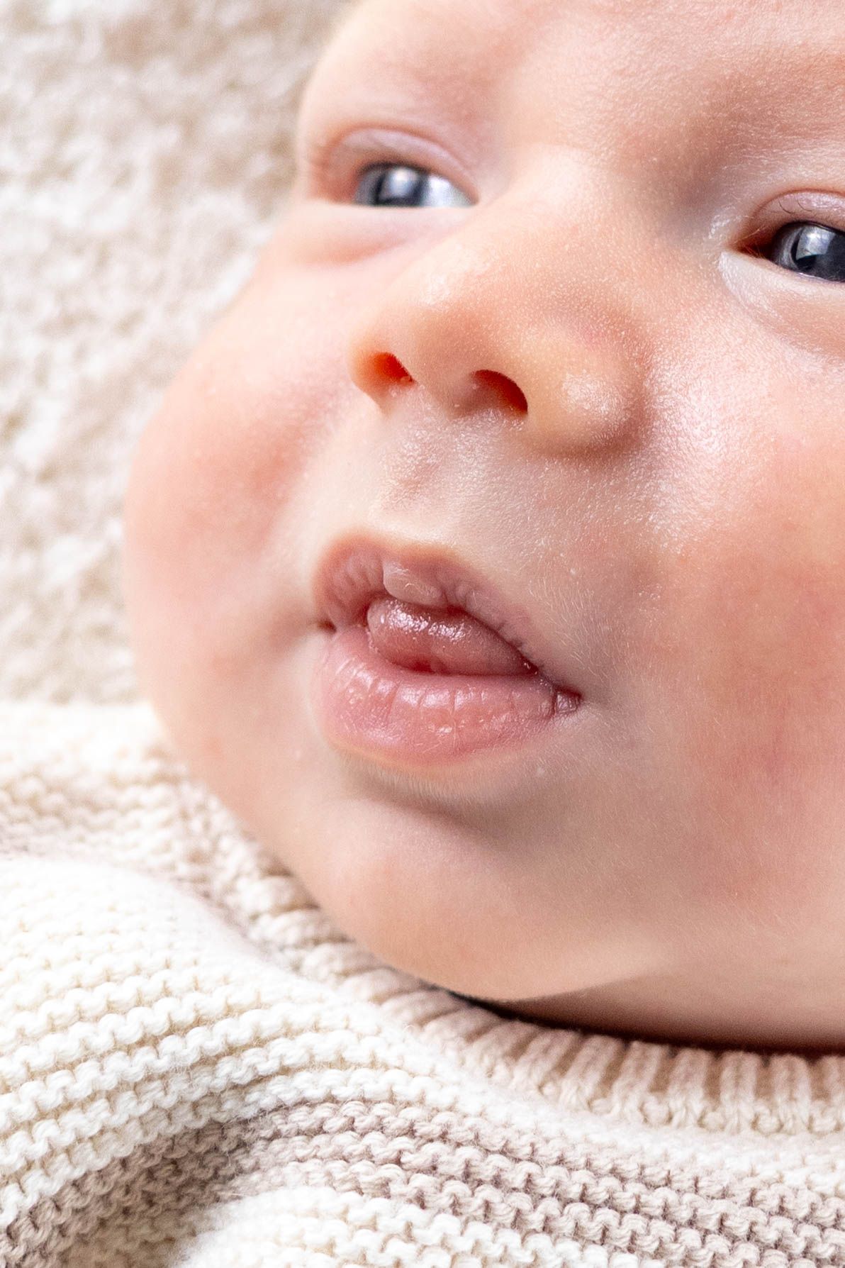 Close-up of baby's face with sweet smile lying on white knitted blanket.