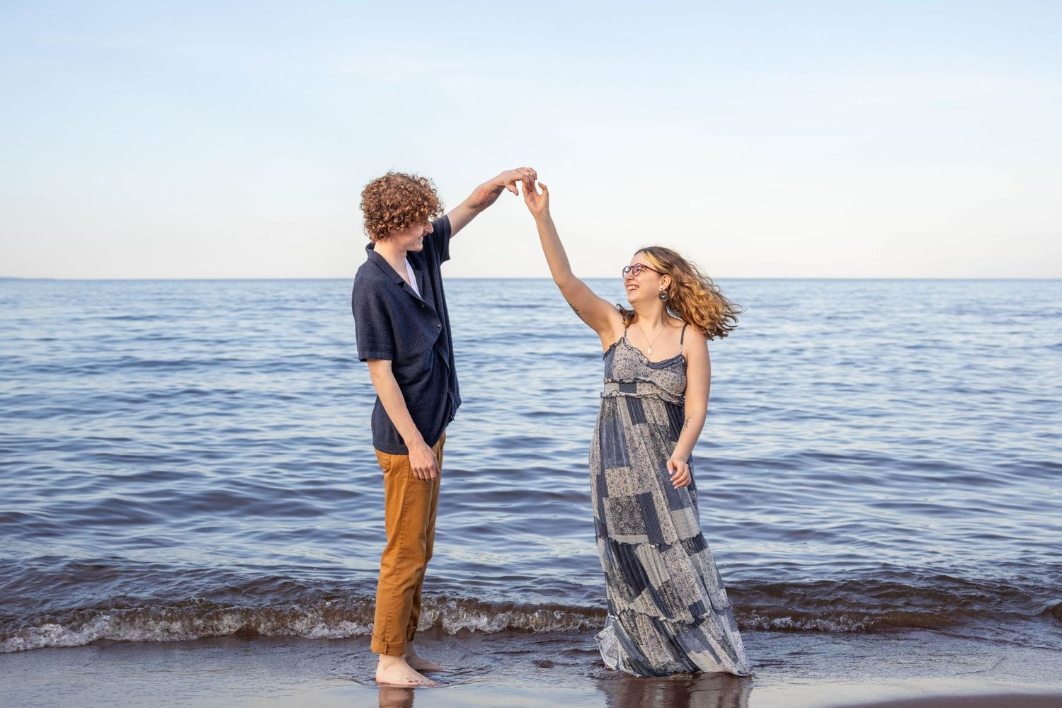Two people dance playfully together at the ocean's edge during sunset, creating silhouettes against the water.