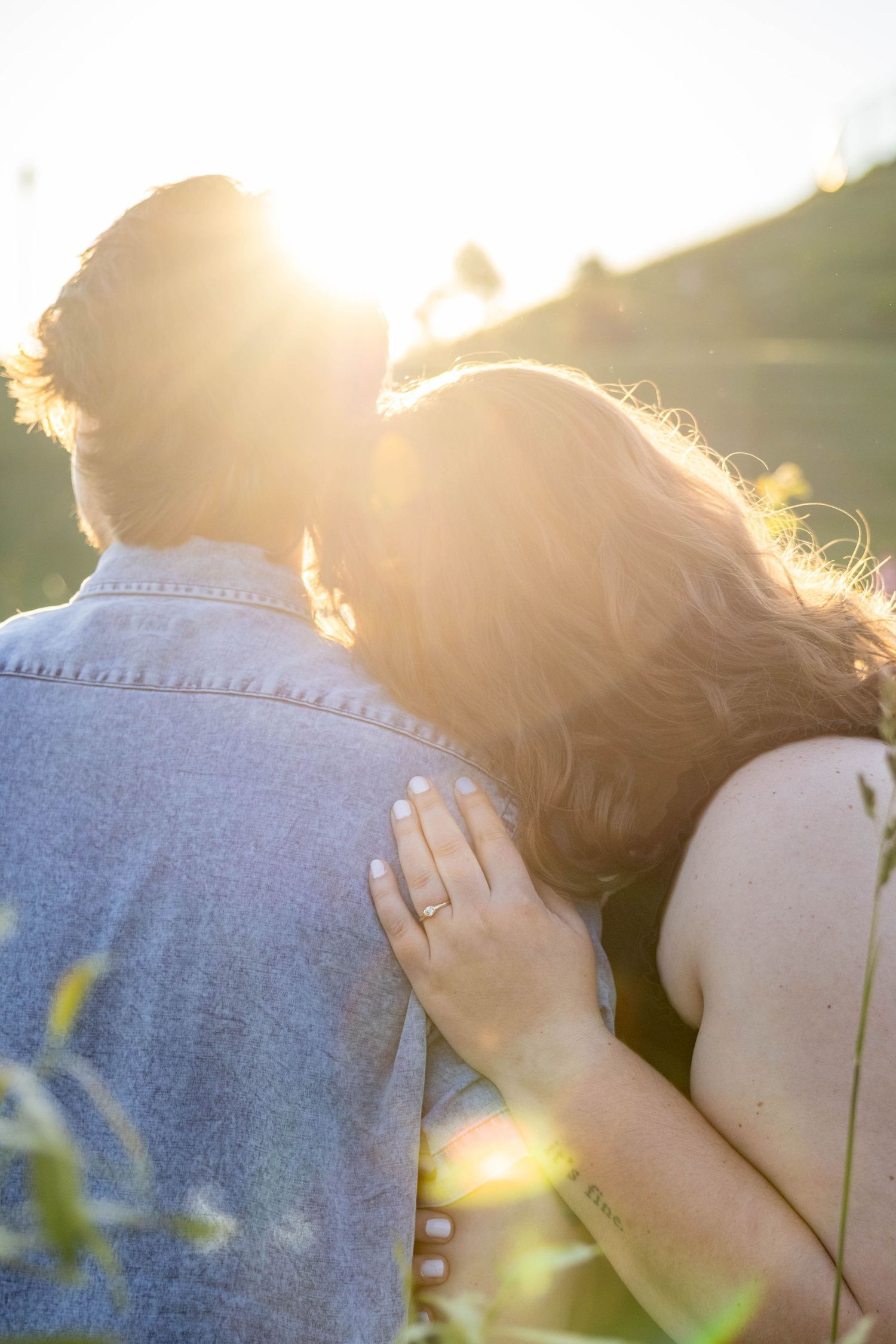Romantic couple embraces in warm sunlight with lens flare creating dreamy golden atmosphere.