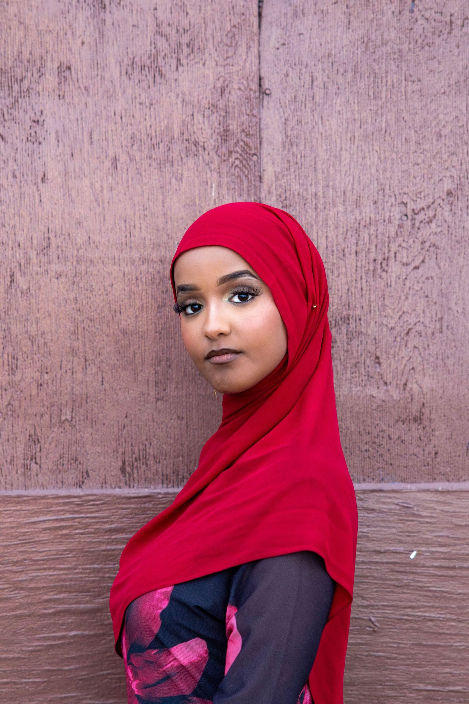 A person wearing a bright red hijab and black top poses against a textured wall in a series of four photos.