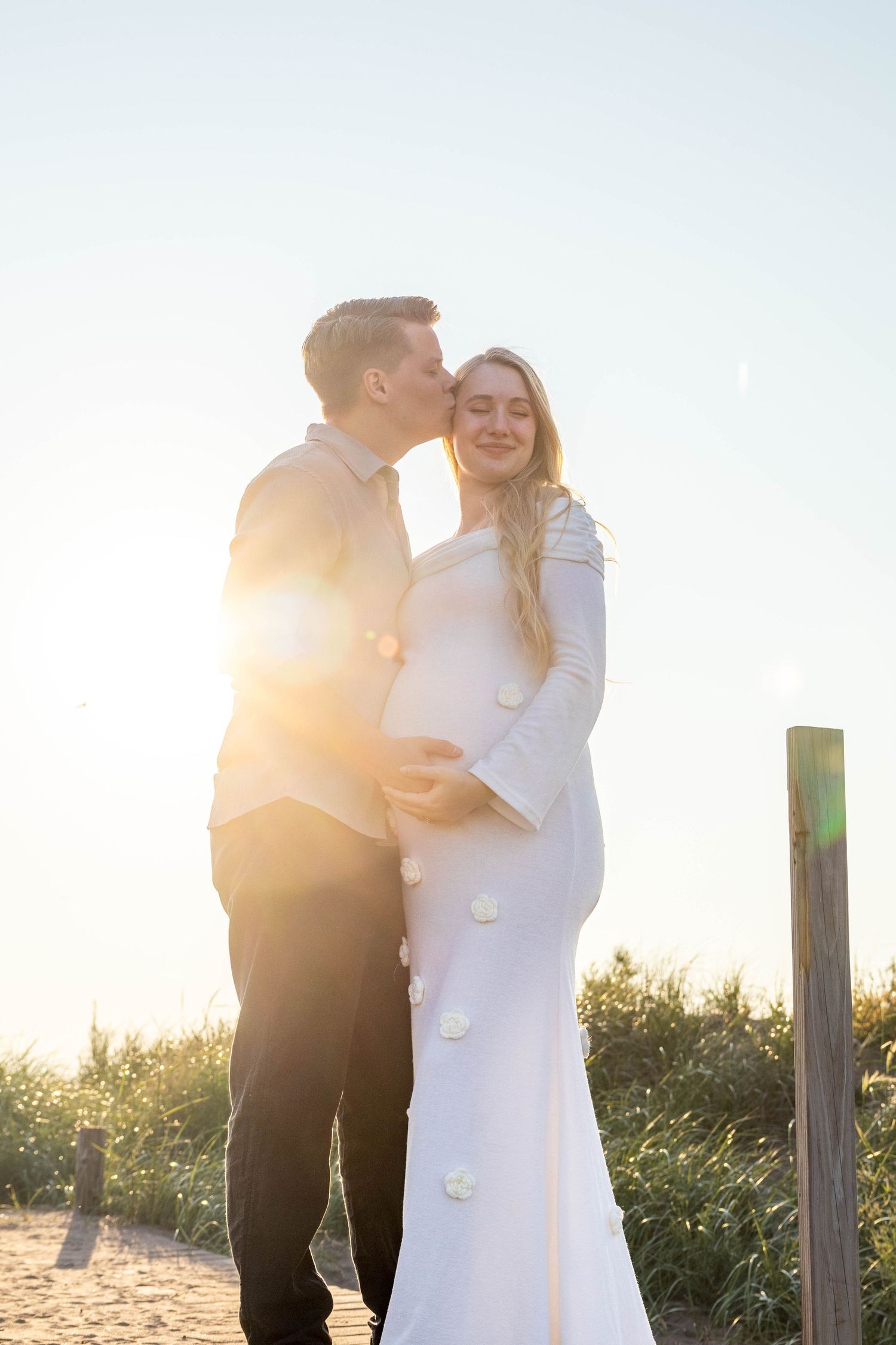 A couple shares romantic moments on a beach boardwalk during golden hour sunset in matching black and white outfits.
