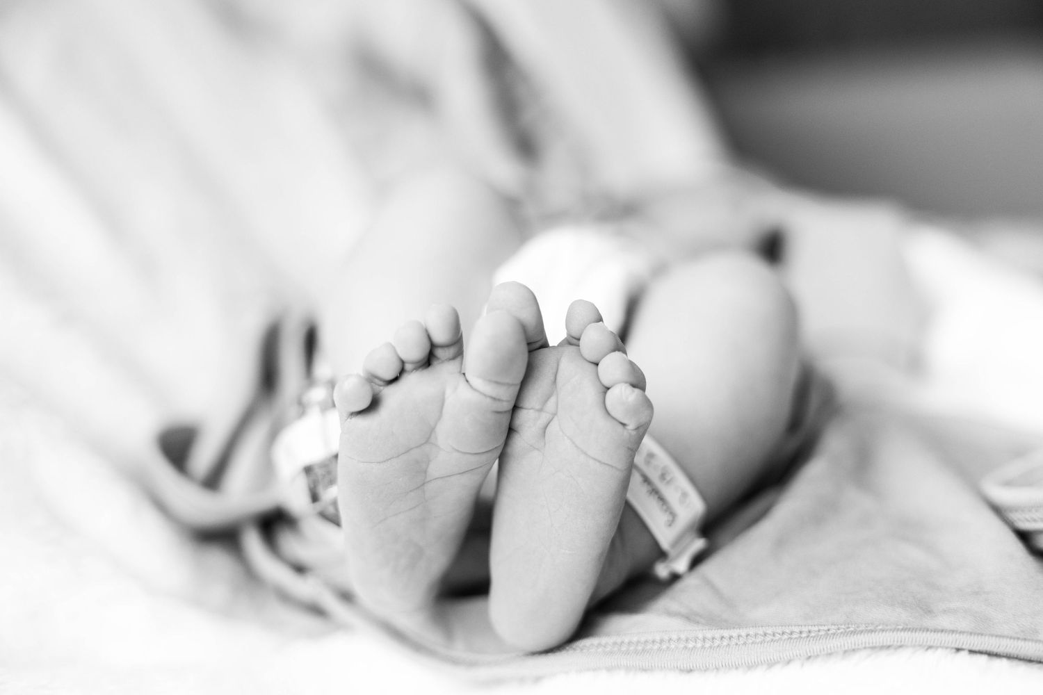 Black and white close-up photograph showing tiny baby feet with delicate toes against a soft blanket.