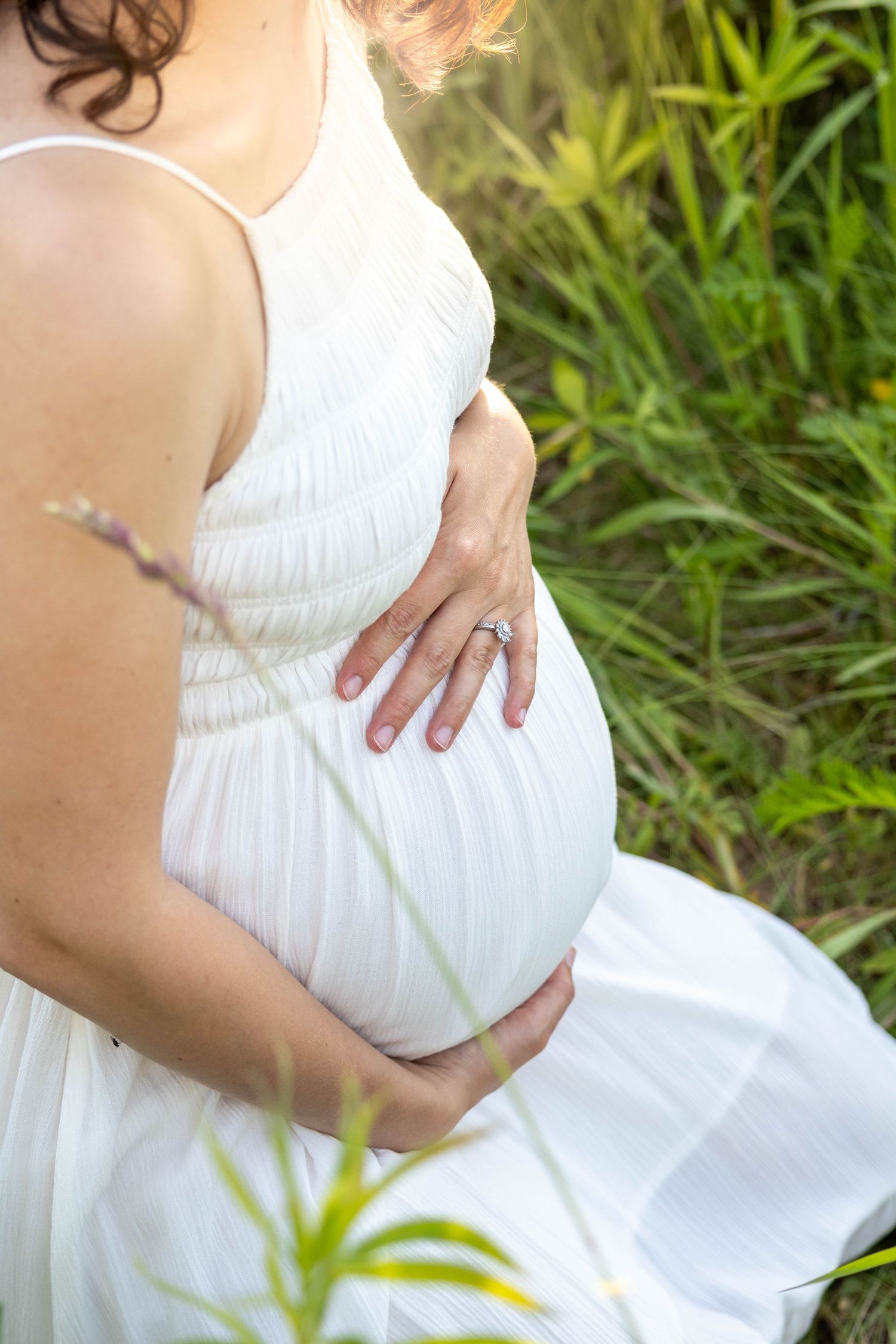 Ethereal maternity photo series showing someone in a white dress tenderly cradling their pregnant belly against a green backdrop.