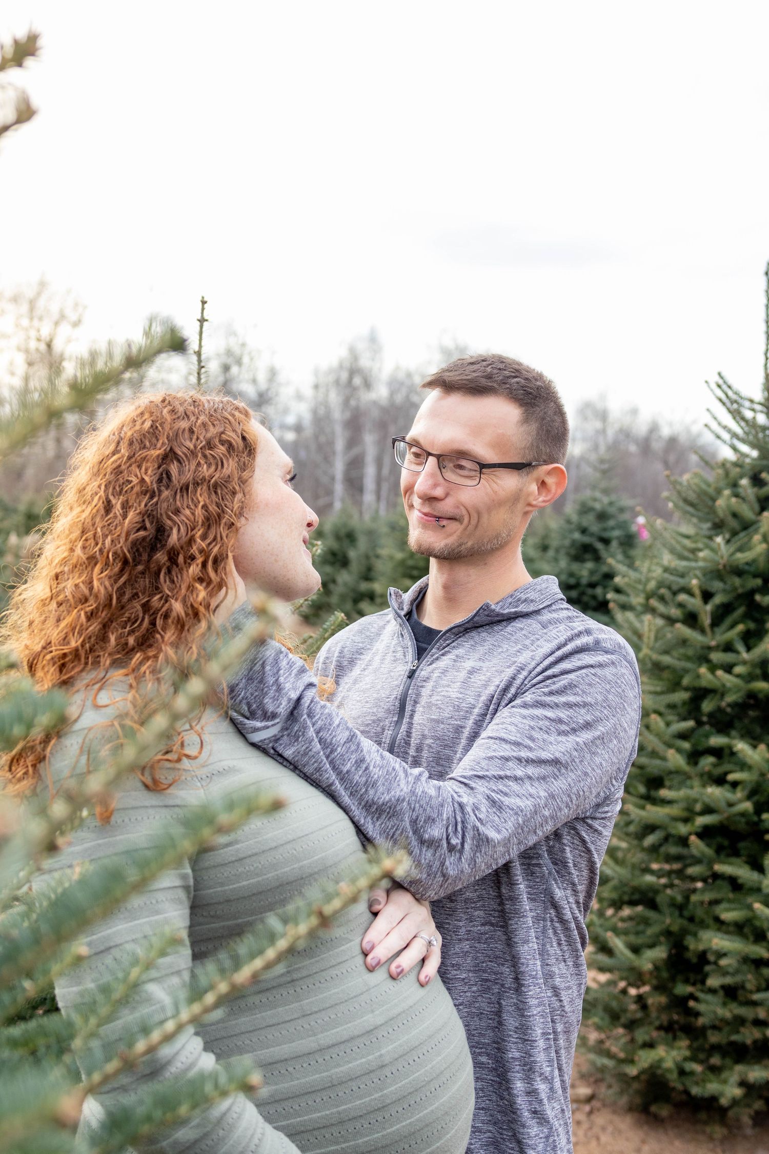 Joyful couple sharing playful moments at a Christmas tree farm surrounded by evergreen trees.
