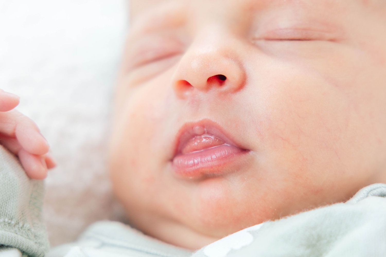 Peaceful sleeping newborn with parted lips against white background.