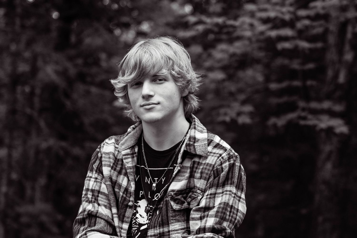 Person in plaid flannel shirt smiling outdoors with dark background.