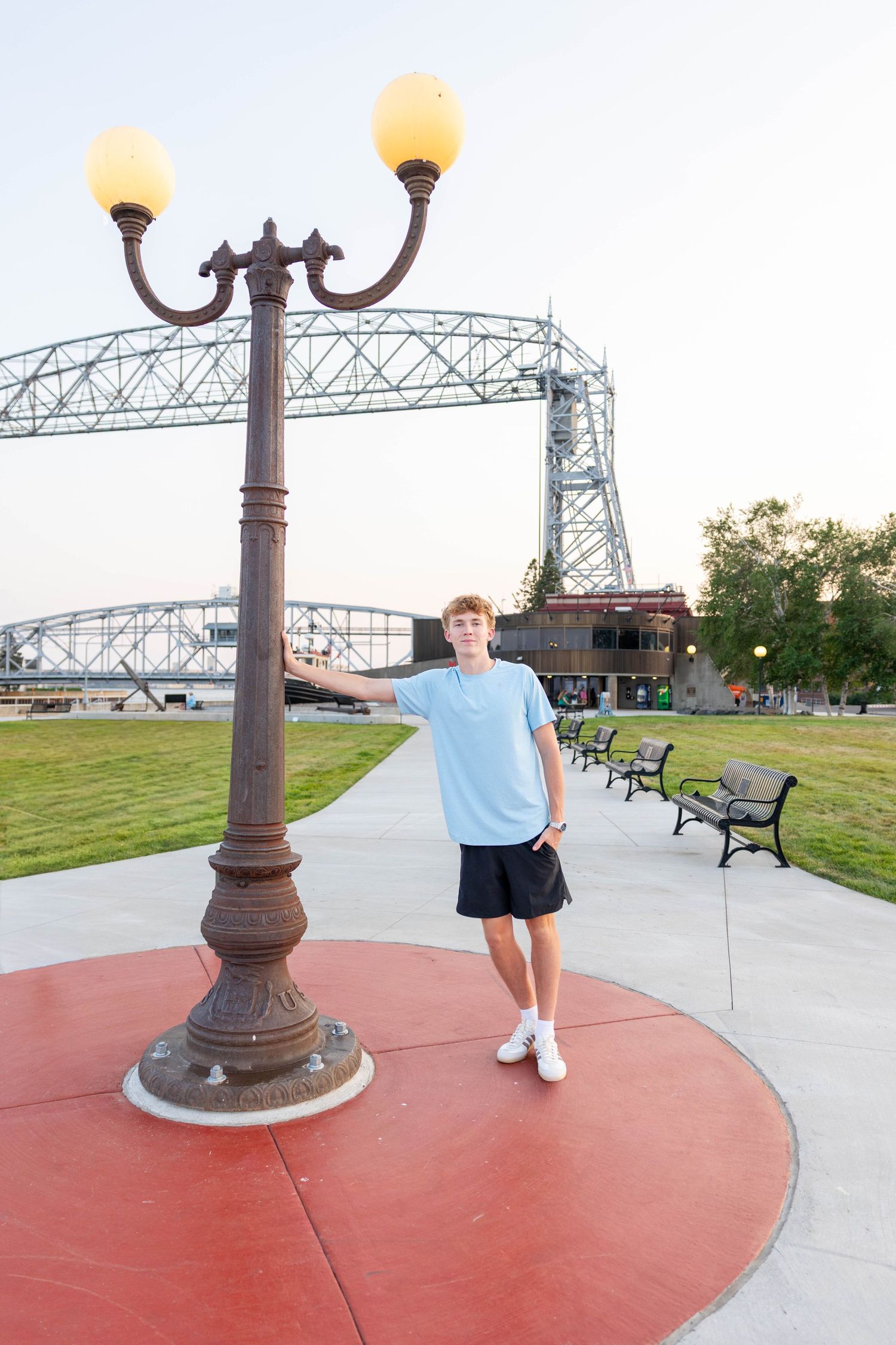 Teen boy leaning on vintage lamp post at Duluth Canal Park with Aerial Lift Bridge in background.