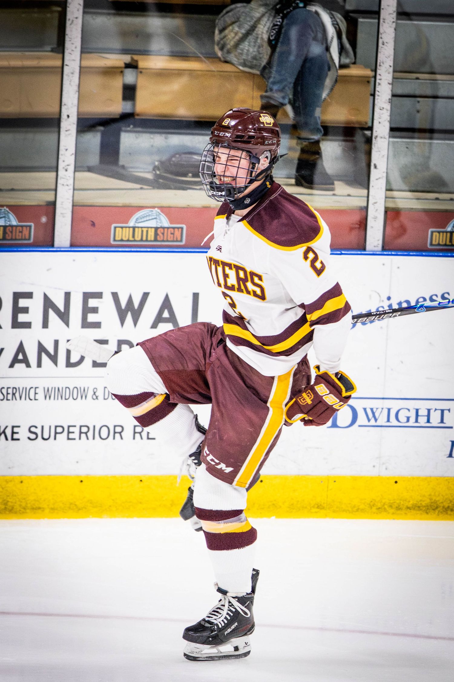 Hockey player in maroon and gold uniform skates on ice rink during game action.