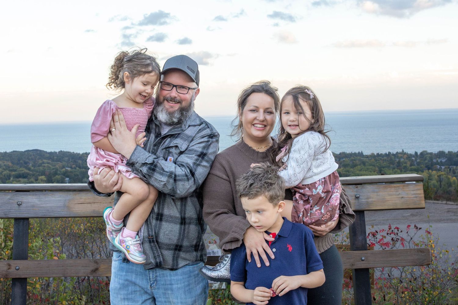 Family portrait session at sunset on a wooden deck overlooking a scenic lake view.