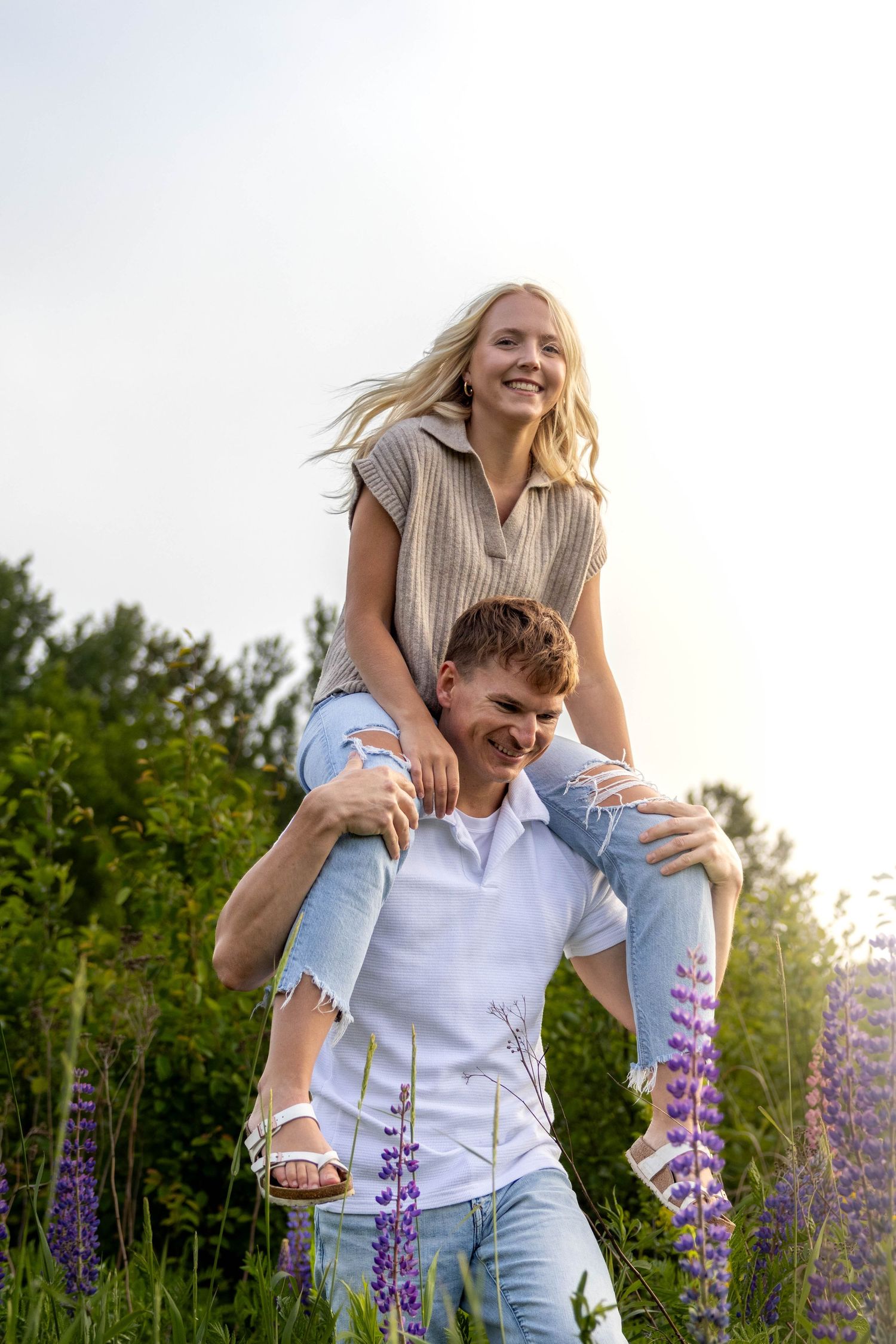 Happy couple enjoying a playful piggyback ride in a field of purple lupine flowers at sunset.