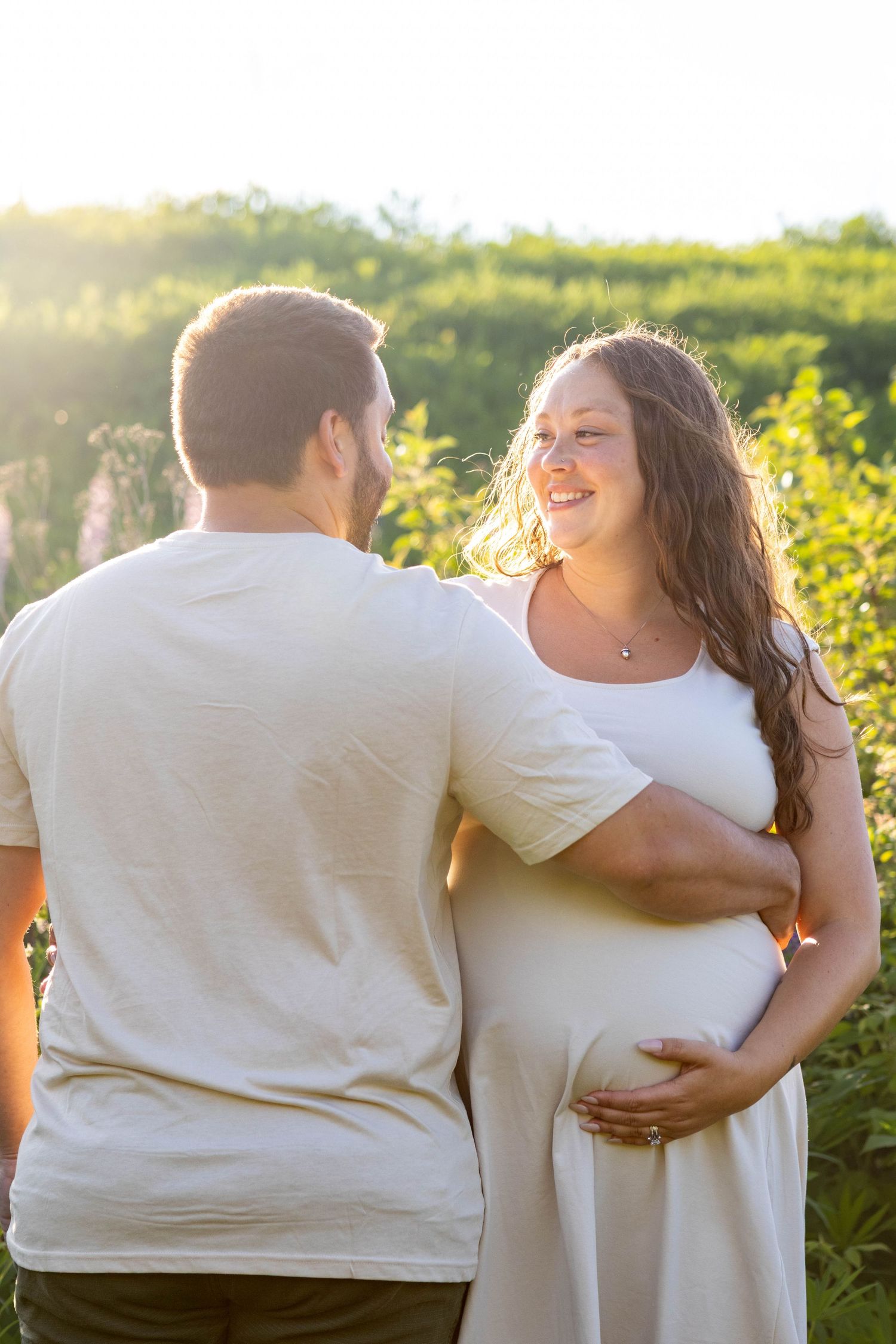 Couple sharing intimate moments together in golden sunlit vineyard while wearing white outfits.