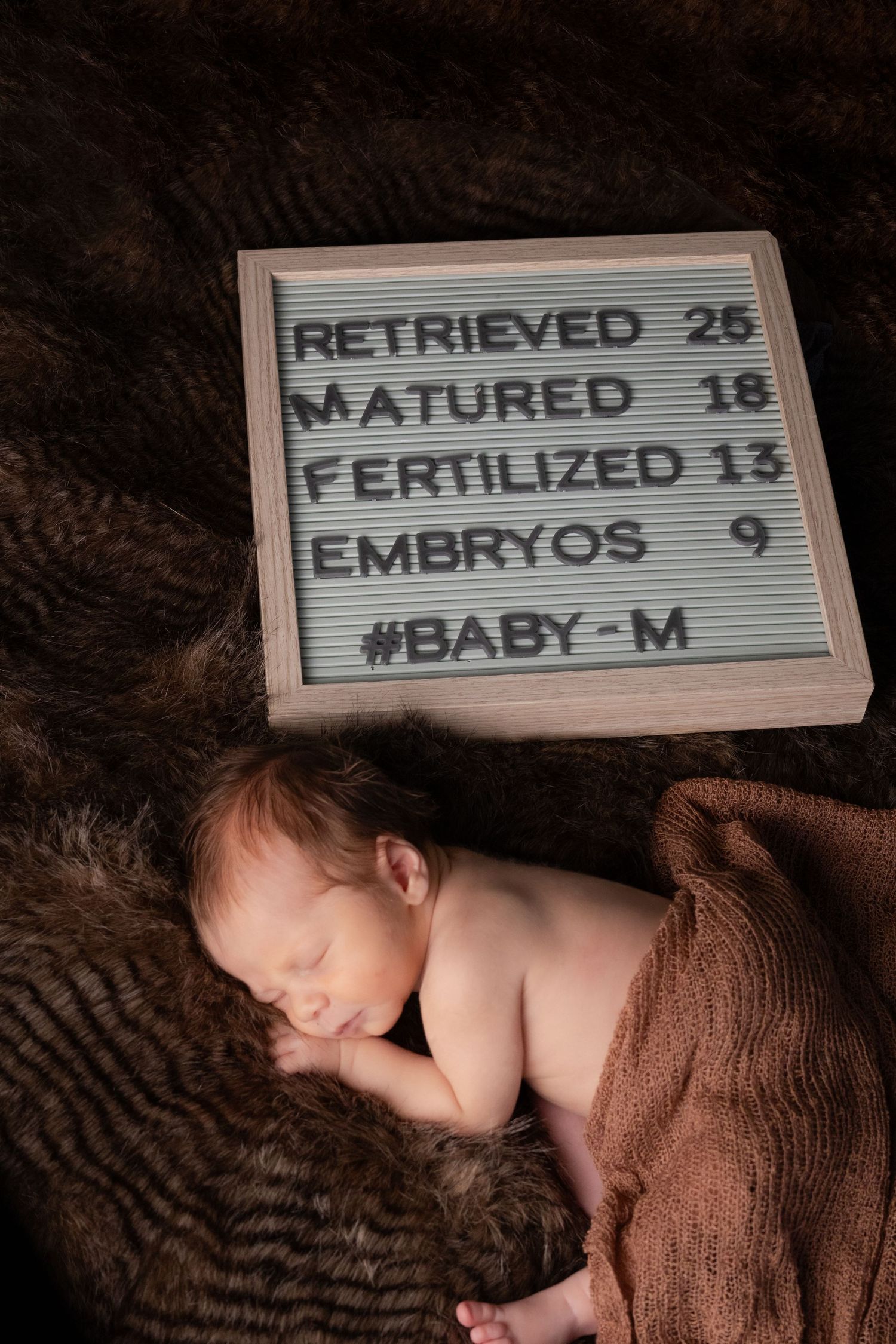 Newborn baby sleeping beside a letter board displaying IVF statistics and journey details.
