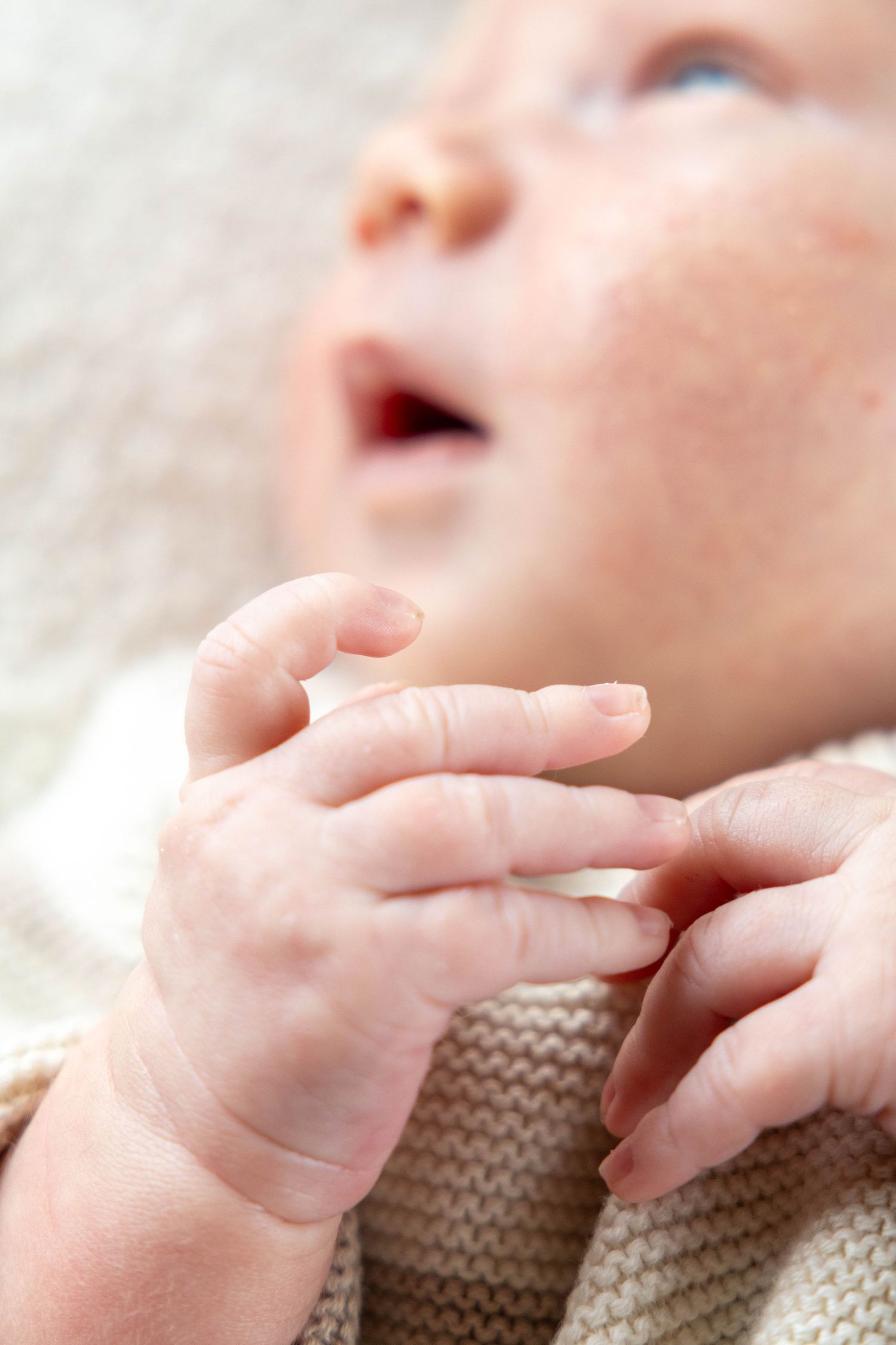 A small baby's hand gently rests on a soft brown knitted blanket or sweater material.