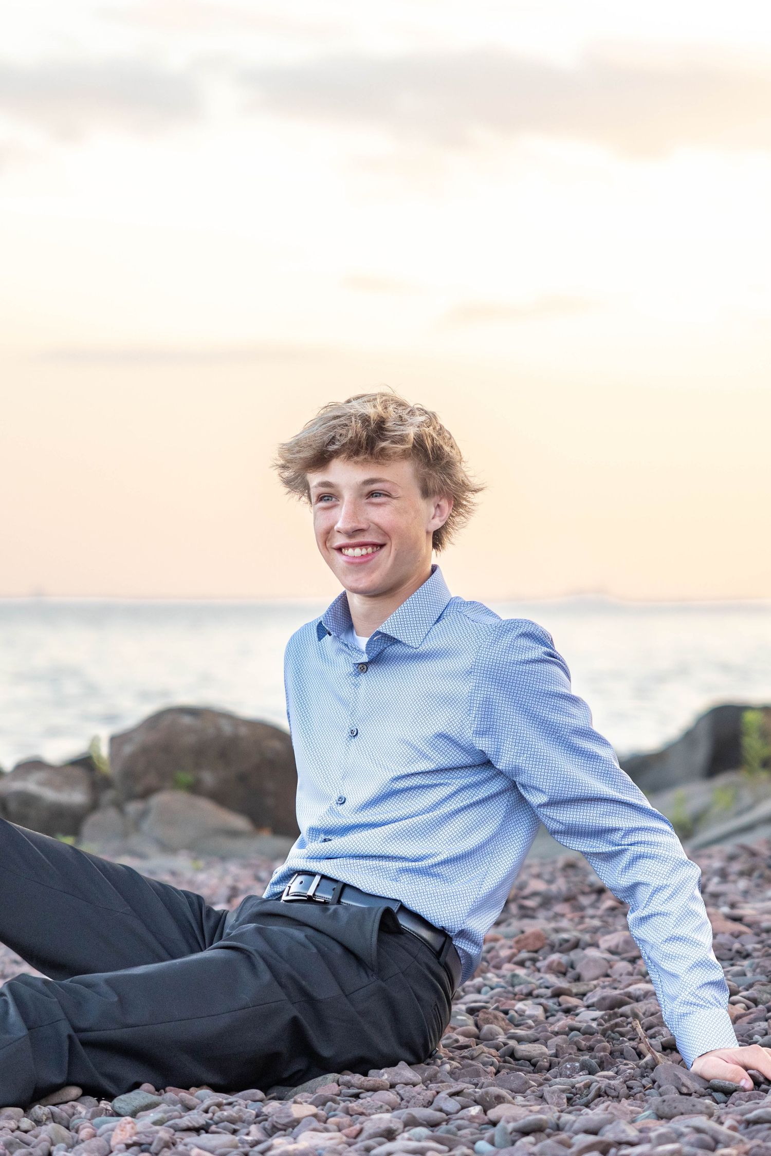 A person in a blue shirt and dark pants relaxes on rocky terrain at sunset.