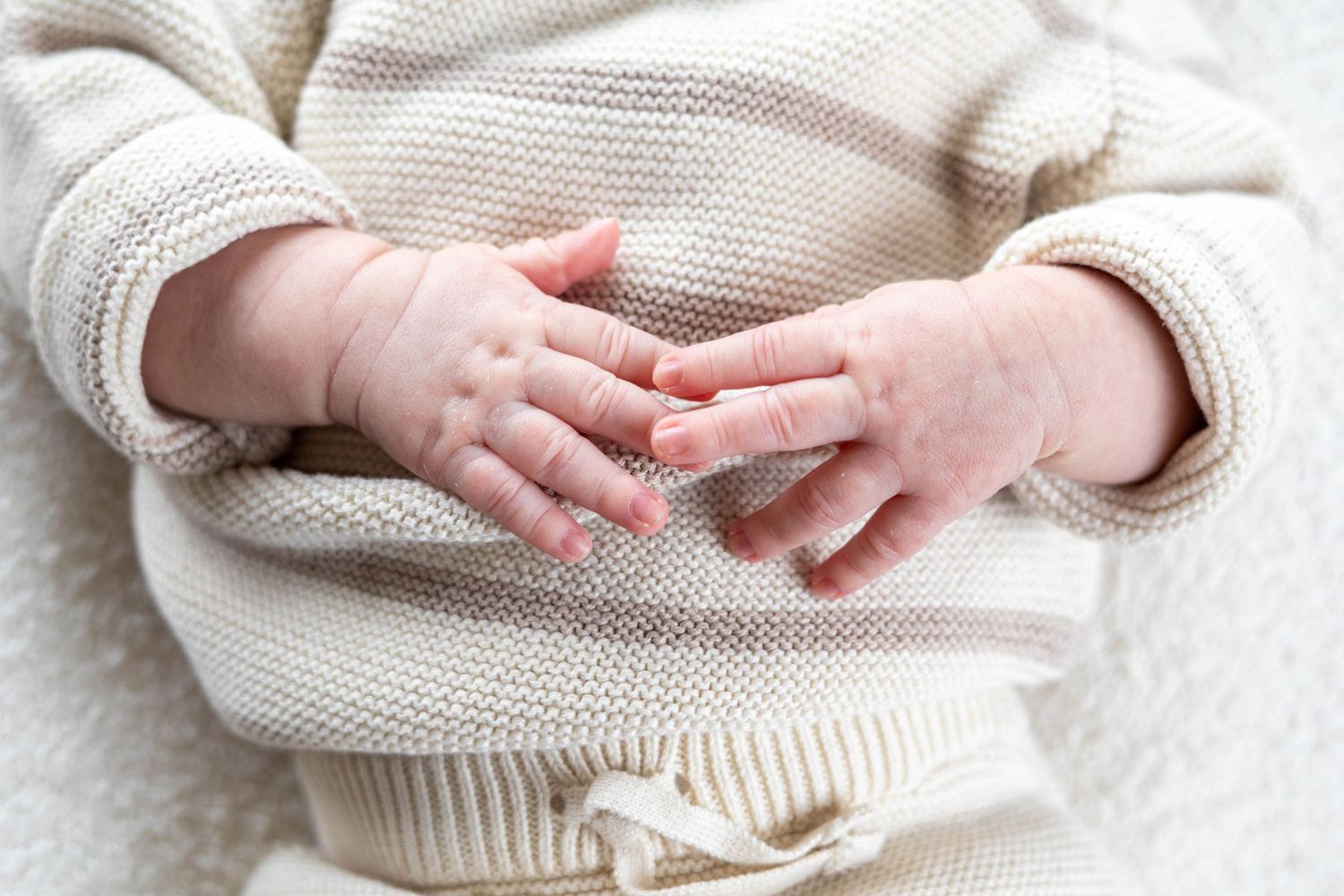 Close up of tiny baby hands touching adult hands against white knit sweater background.