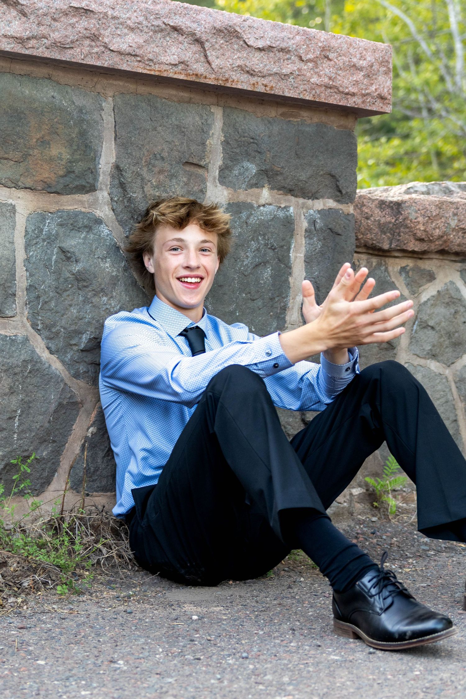 A person in a blue shirt and dark pants lies playfully under a stone wall in a sequence of five similar poses.